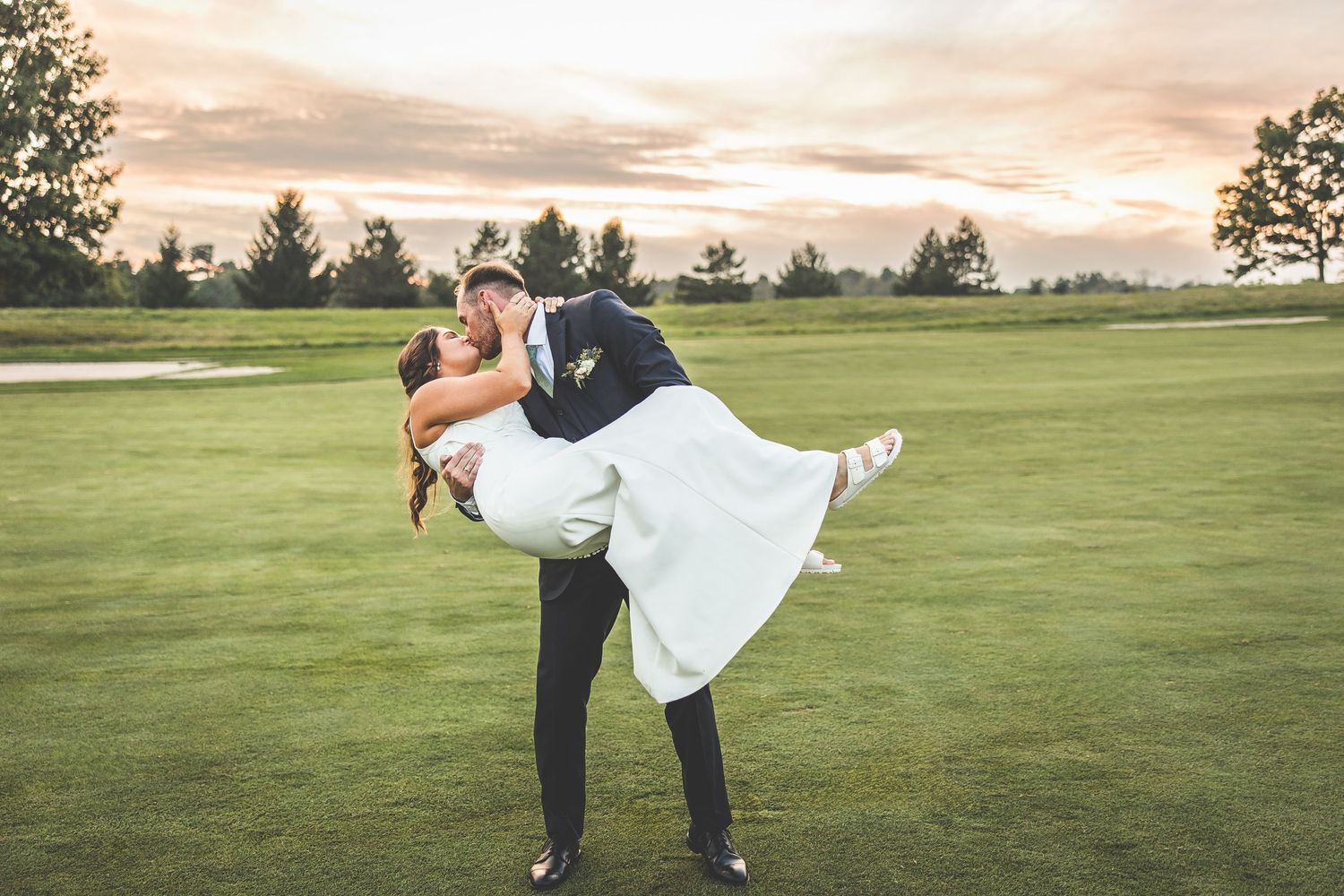 Couple dancing together on a green lawn at sunset during an outdoor wedding celebration.