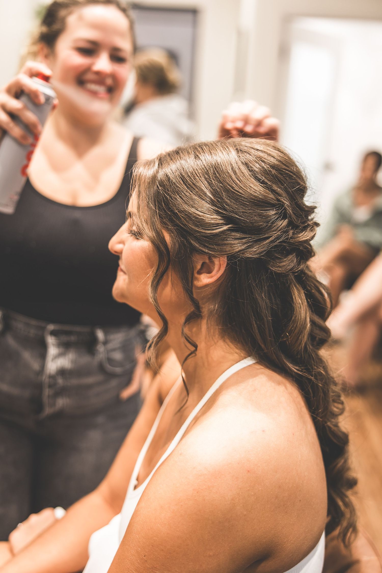 A group of women laugh joyfully together during a wedding preparation, wearing elegant hairstyles.