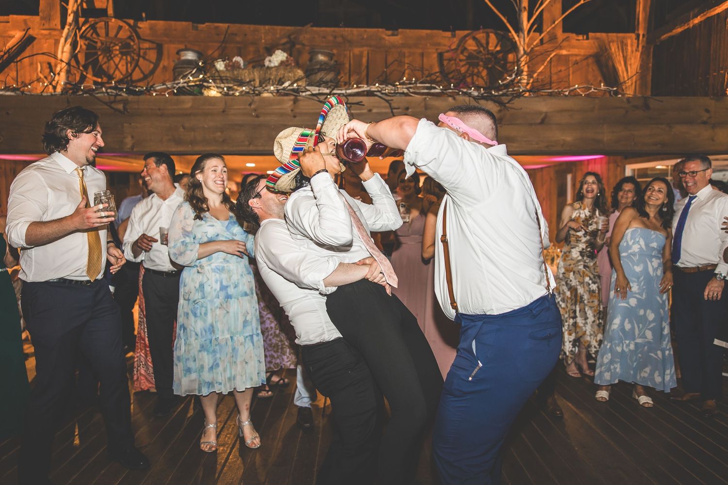 Lively dance floor scene at a wedding reception with guests celebrating in a rustic venue.