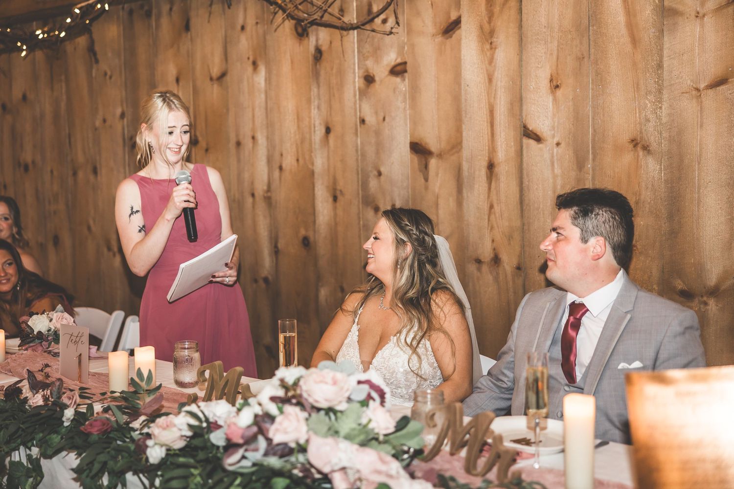 Wedding reception tables set in rustic barn venue with floral centerpieces and candlelight.