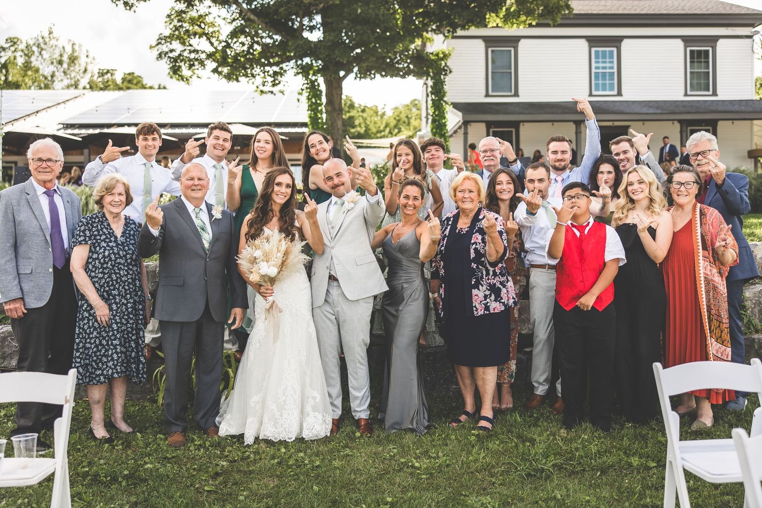 Large wedding party group photo taken outdoors with guests lined up in front of a house.