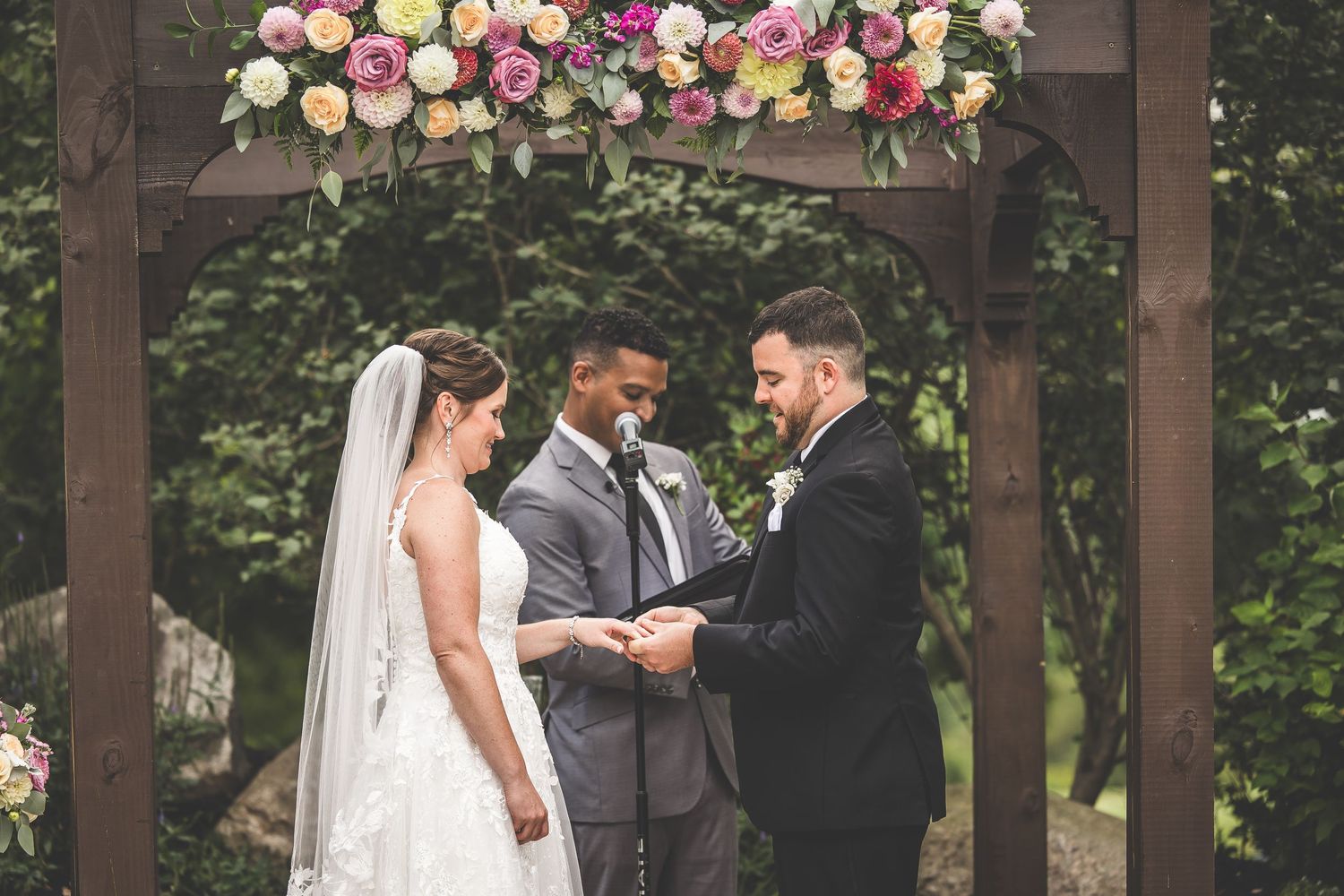 Intimate wedding ceremony moments under wooden pergola with pink and white flowers.