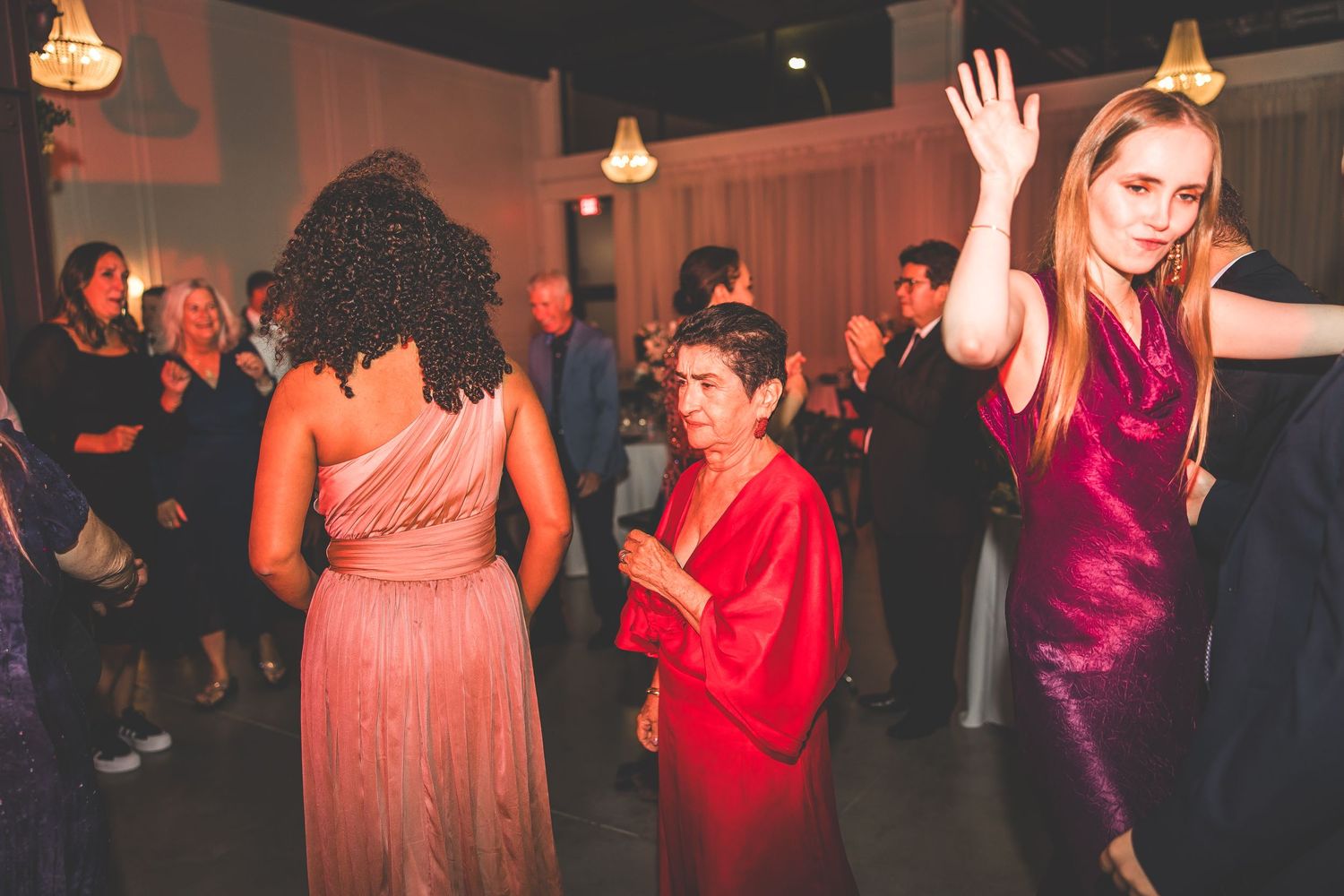 Wedding party dancing and celebrating at a lively reception with red ambient lighting.