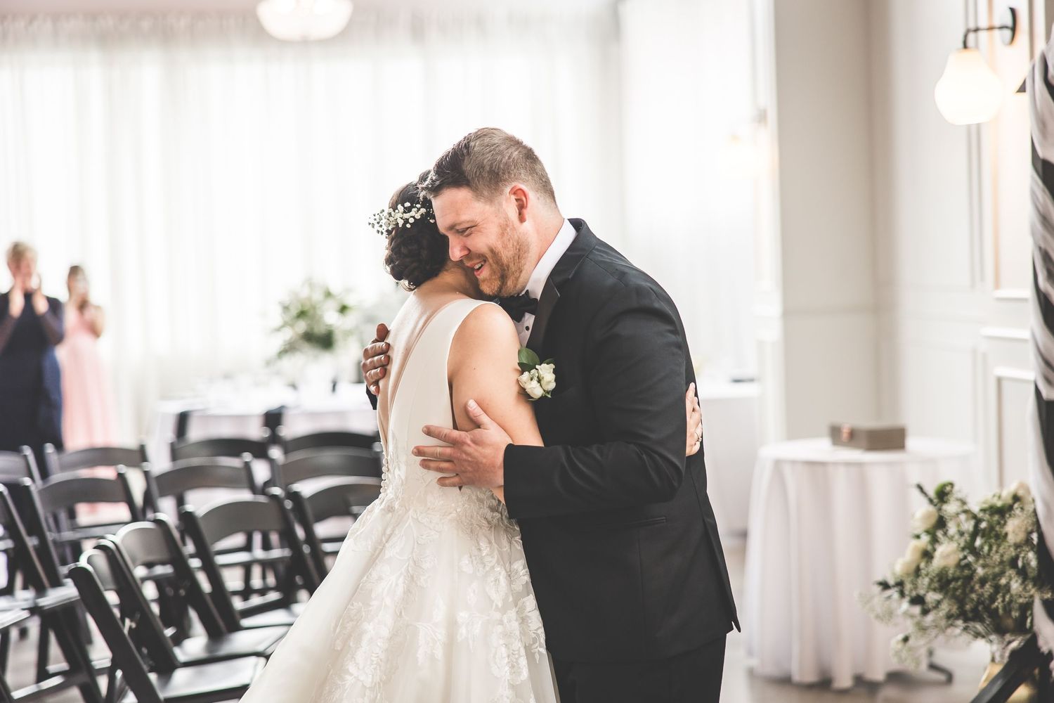 Tender wedding moment captured in a bright venue with rows of black chairs.