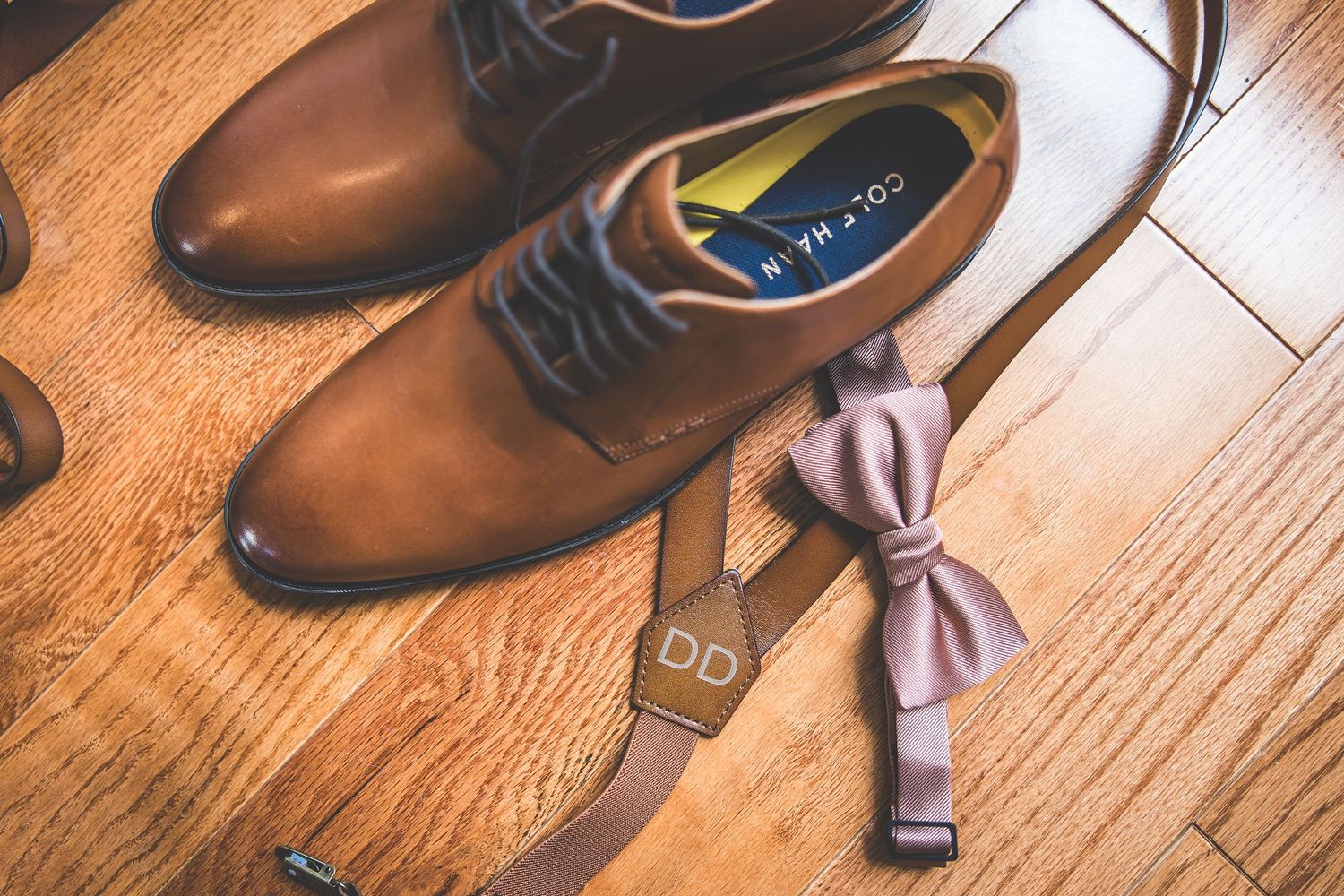 Brown leather dress shoes arranged on wooden floor for wedding preparation.