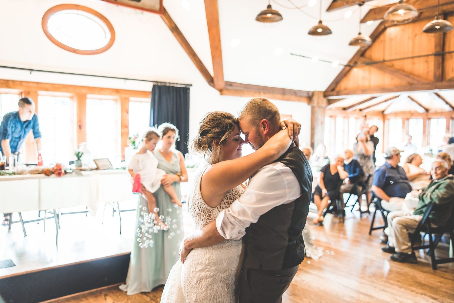 Wedding reception dance floor filled with guests celebrating under rustic wooden beams.