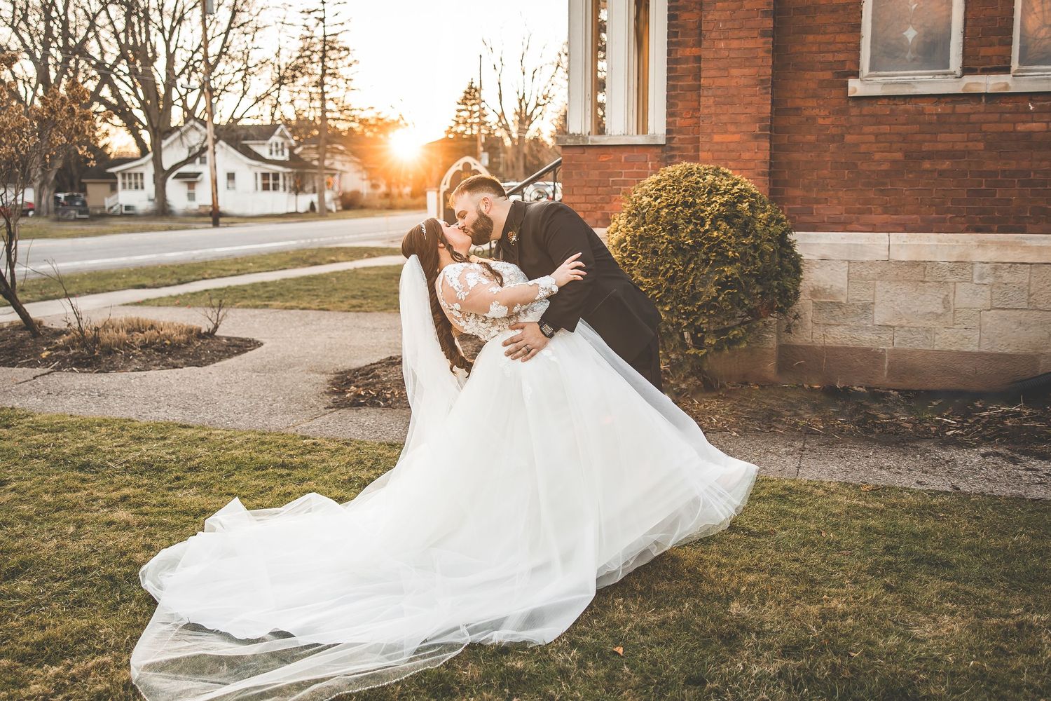 White wedding dress flowing in the golden sunlight against a brick building backdrop.