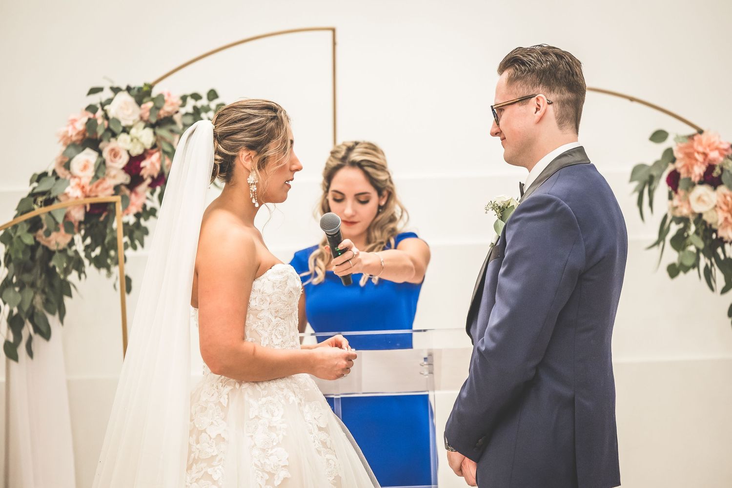 Intimate wedding ceremony moments under floral copper arch in white venue.