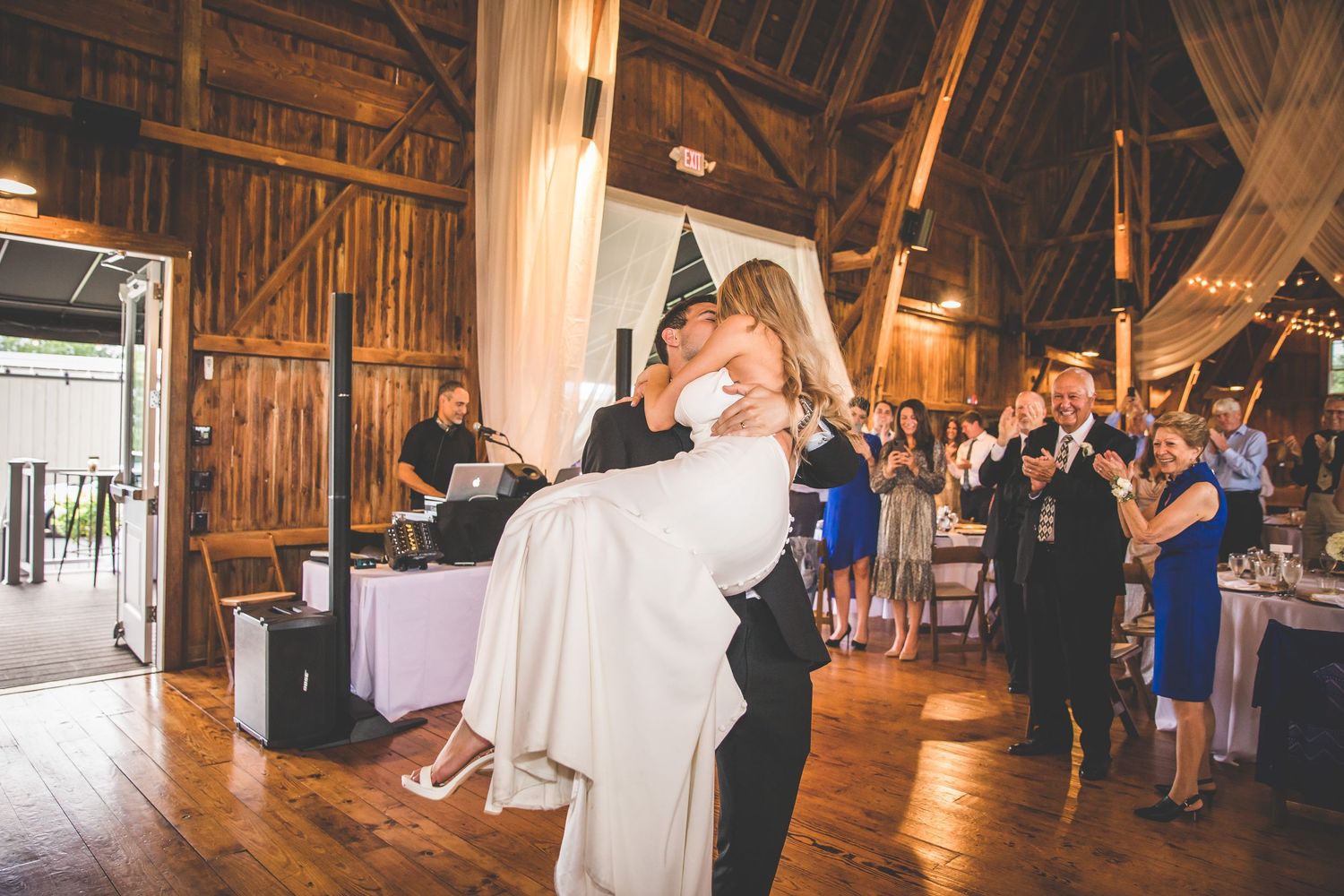 Romantic dance moment in rustic barn reception with guests watching.