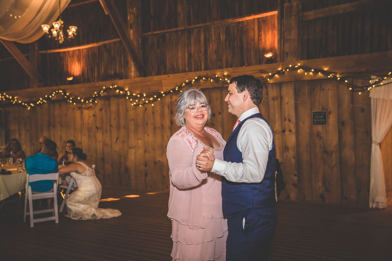 Couples dancing together in a rustic barn venue decorated with warm string lights.