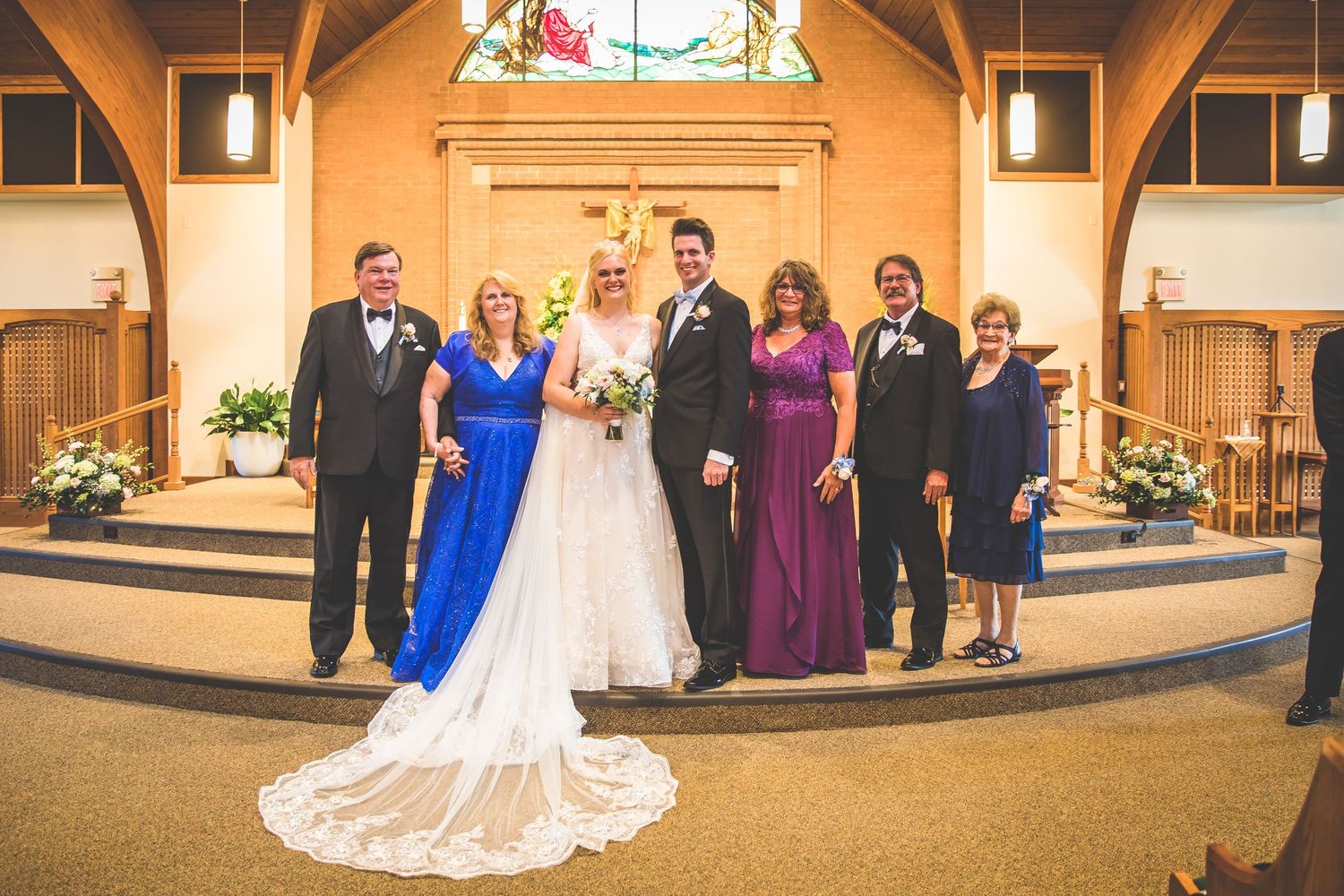 Wedding party stands together in church sanctuary with stained glass window and wooden beams.