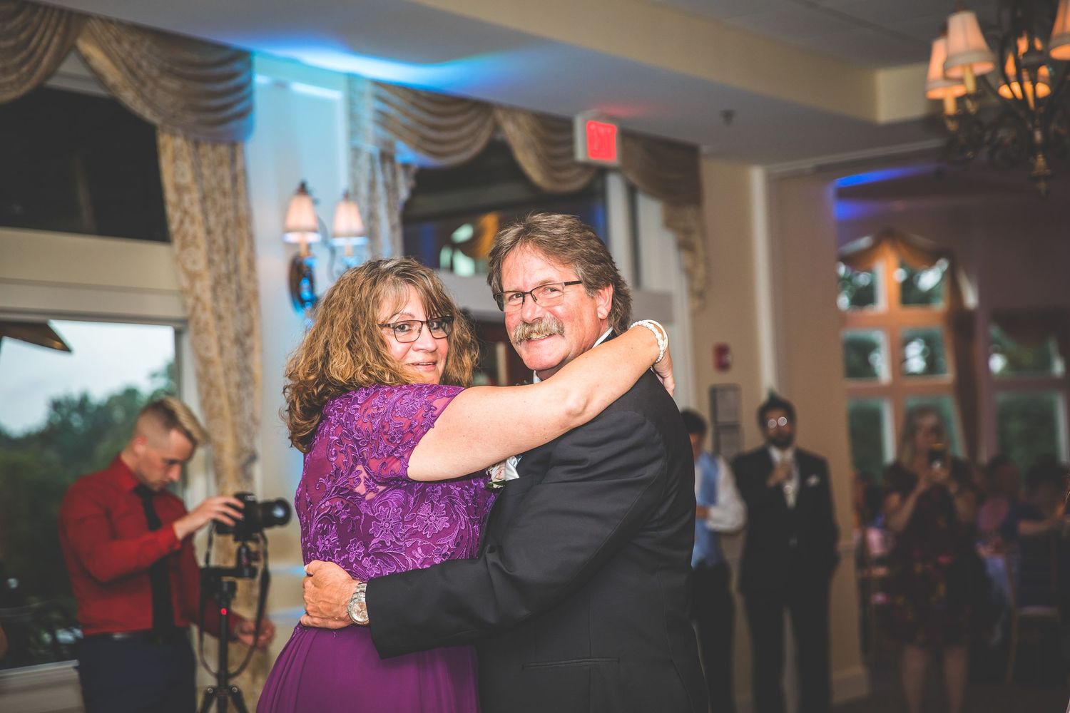 Wedding reception dance with blue uplighting and elegant window treatments in background.