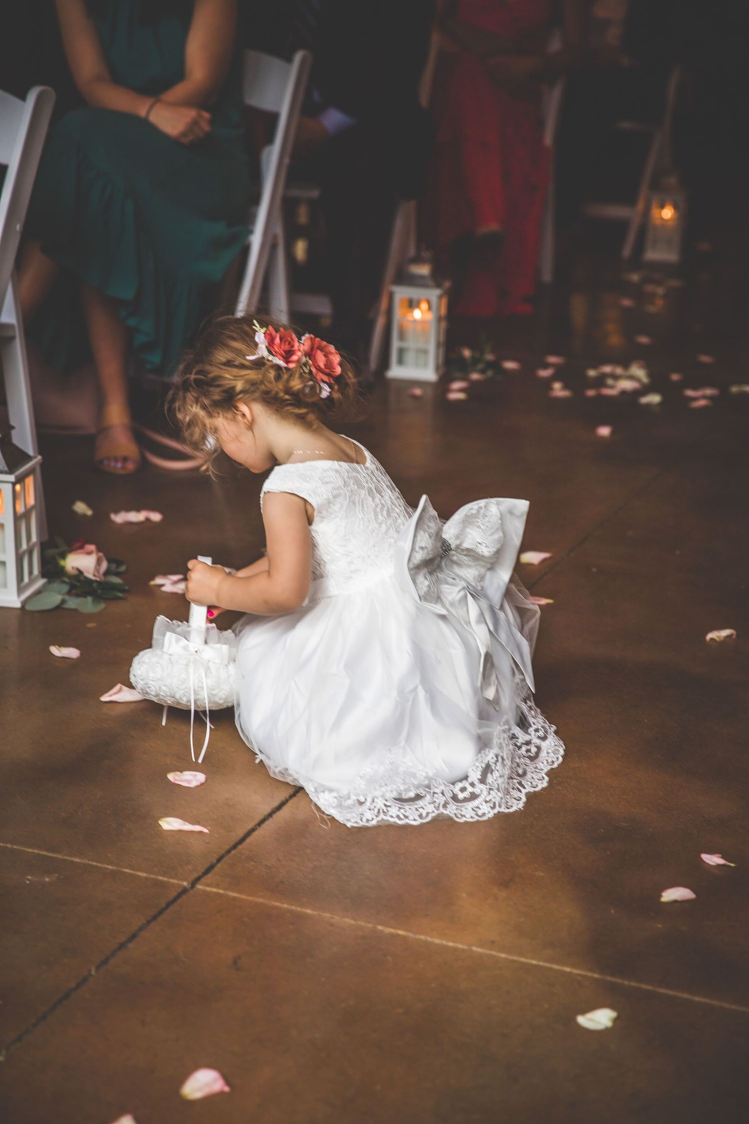 White wedding dress spread out on dark wooden dance floor with scattered rose petals.