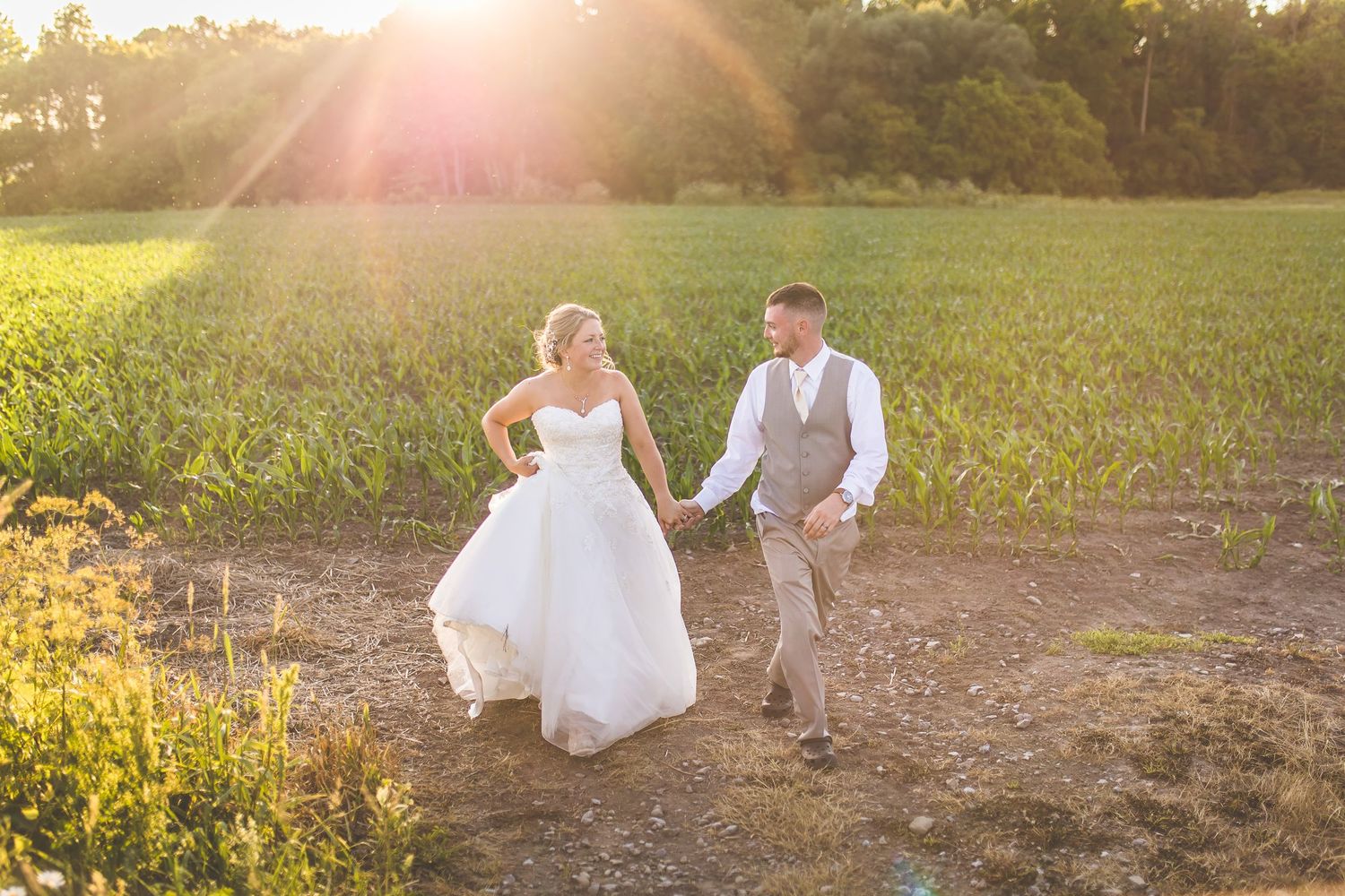 Couple walking hand in hand through a sunlit field during their wedding.