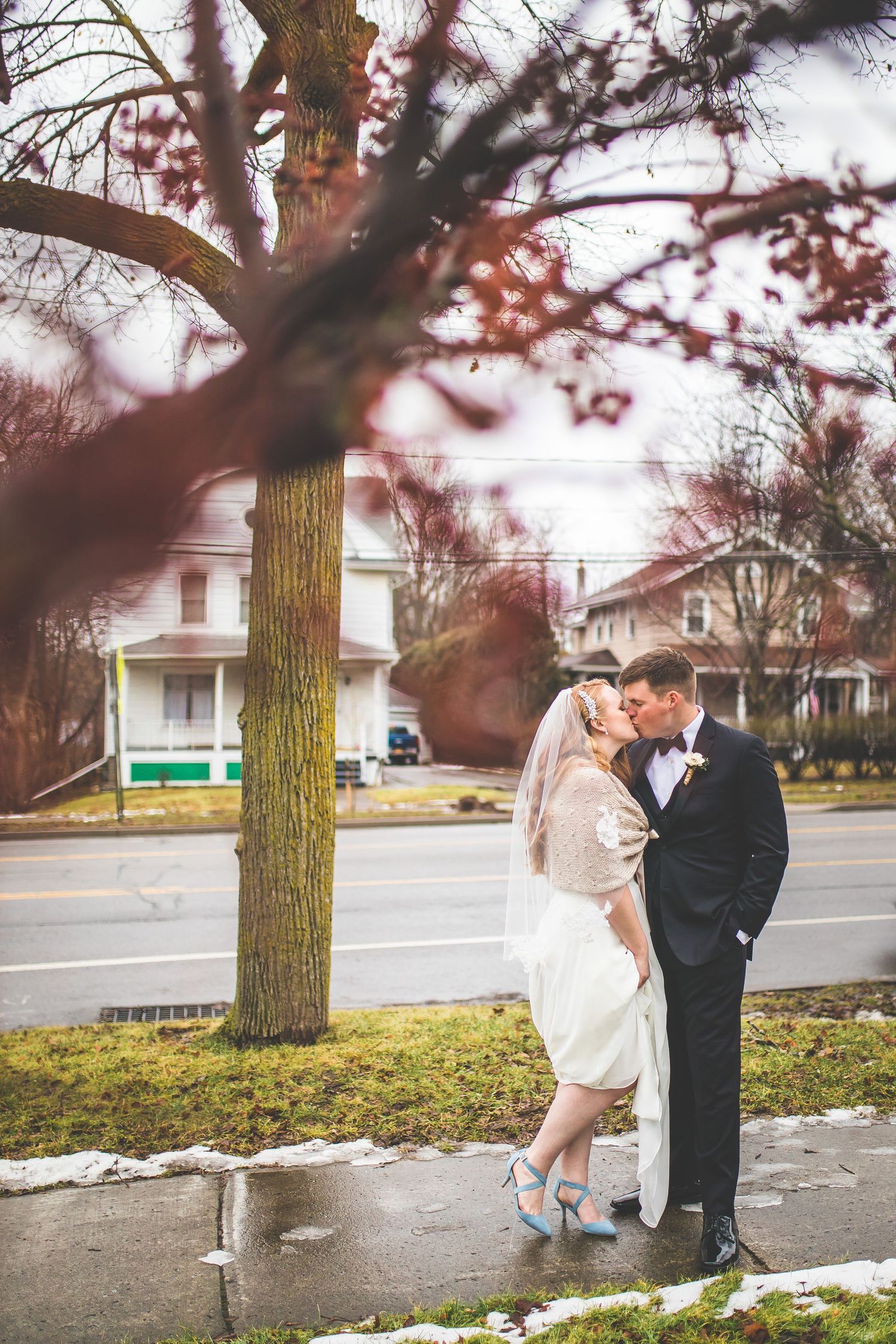Winter wedding couple poses romantically under bare trees with snow on ground.