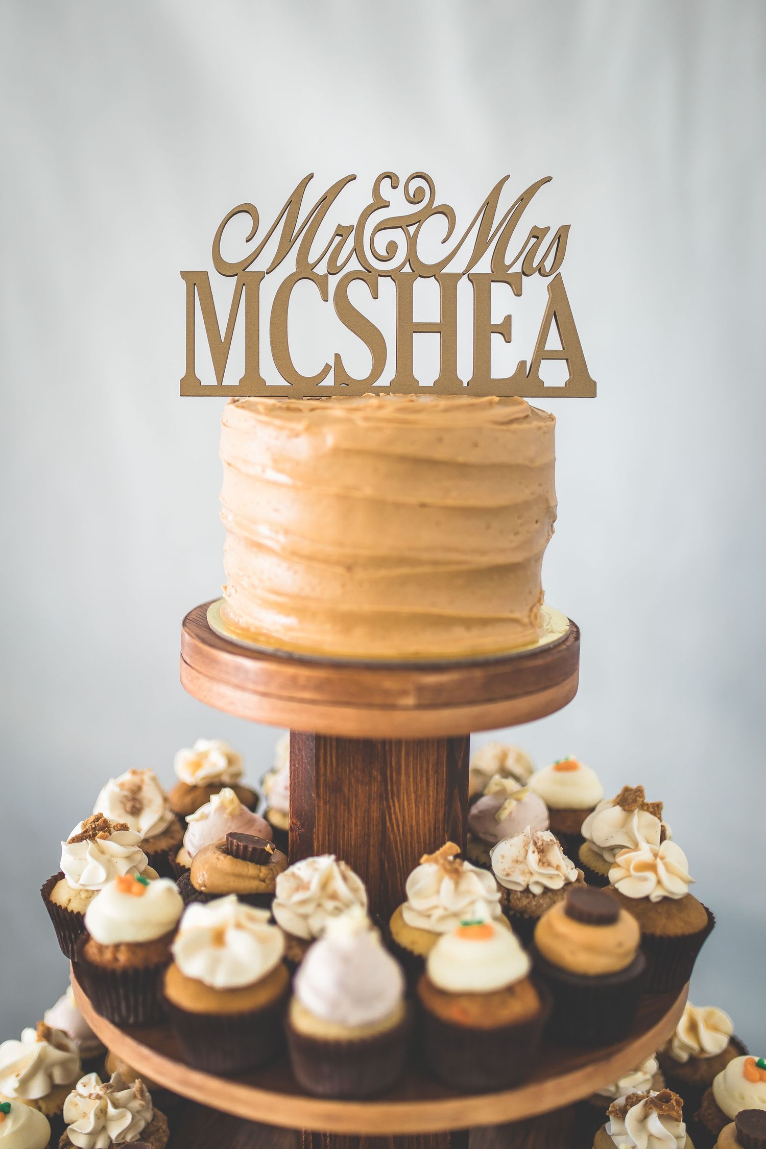 Rustic wedding cake display with Mr & Mrs topper and cupcakes arranged on wooden stands.