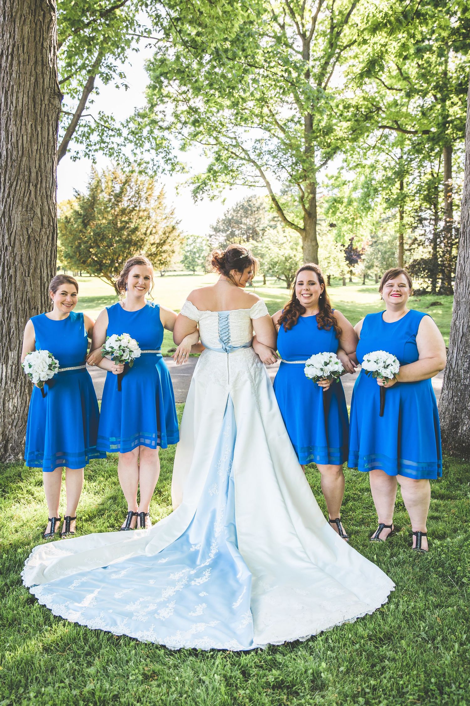 Bridesmaids in royal blue dresses pose with the bride showing off her flowing train.