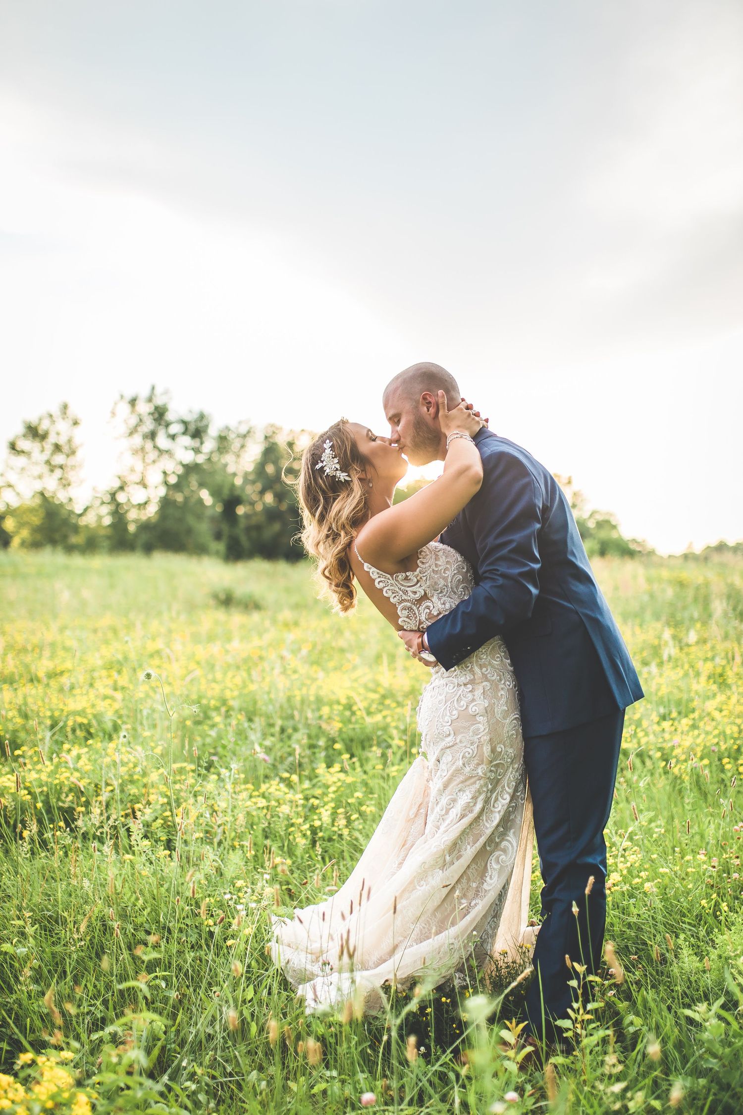 A couple shares an intimate moment in a sunlit meadow with wildflowers during their wedding photoshoot.