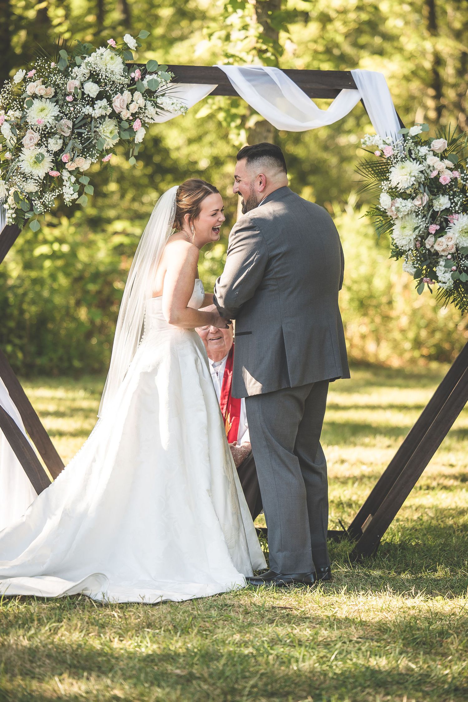 An intimate wedding ceremony scene with elegant floral decorations and flowing white fabric.