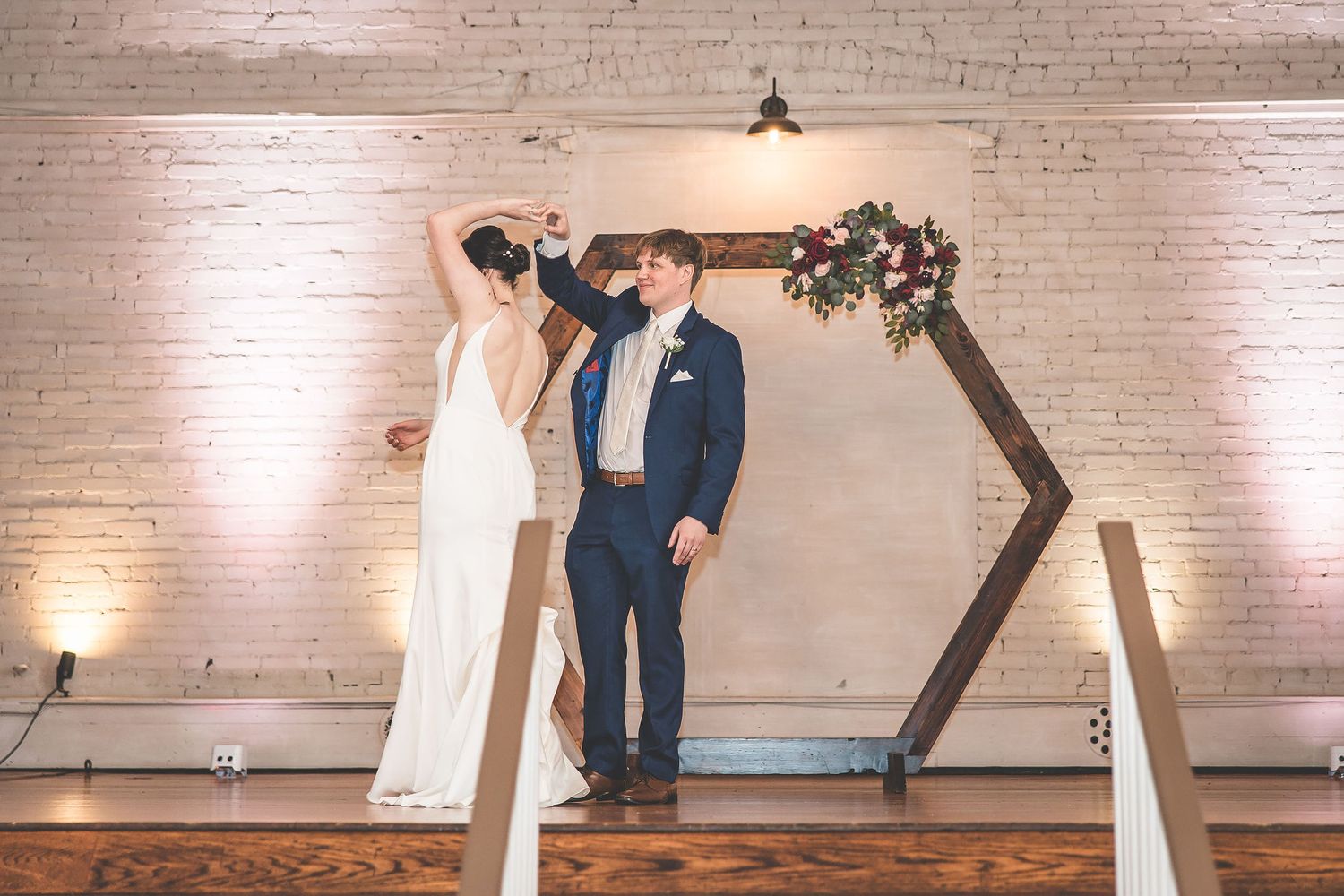 Wedding couple shares a romantic dance moment in front of a geometric wooden backdrop.