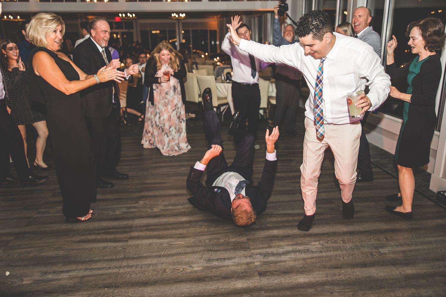 Wedding guests dance energetically on a wooden dance floor during a lively reception celebration.