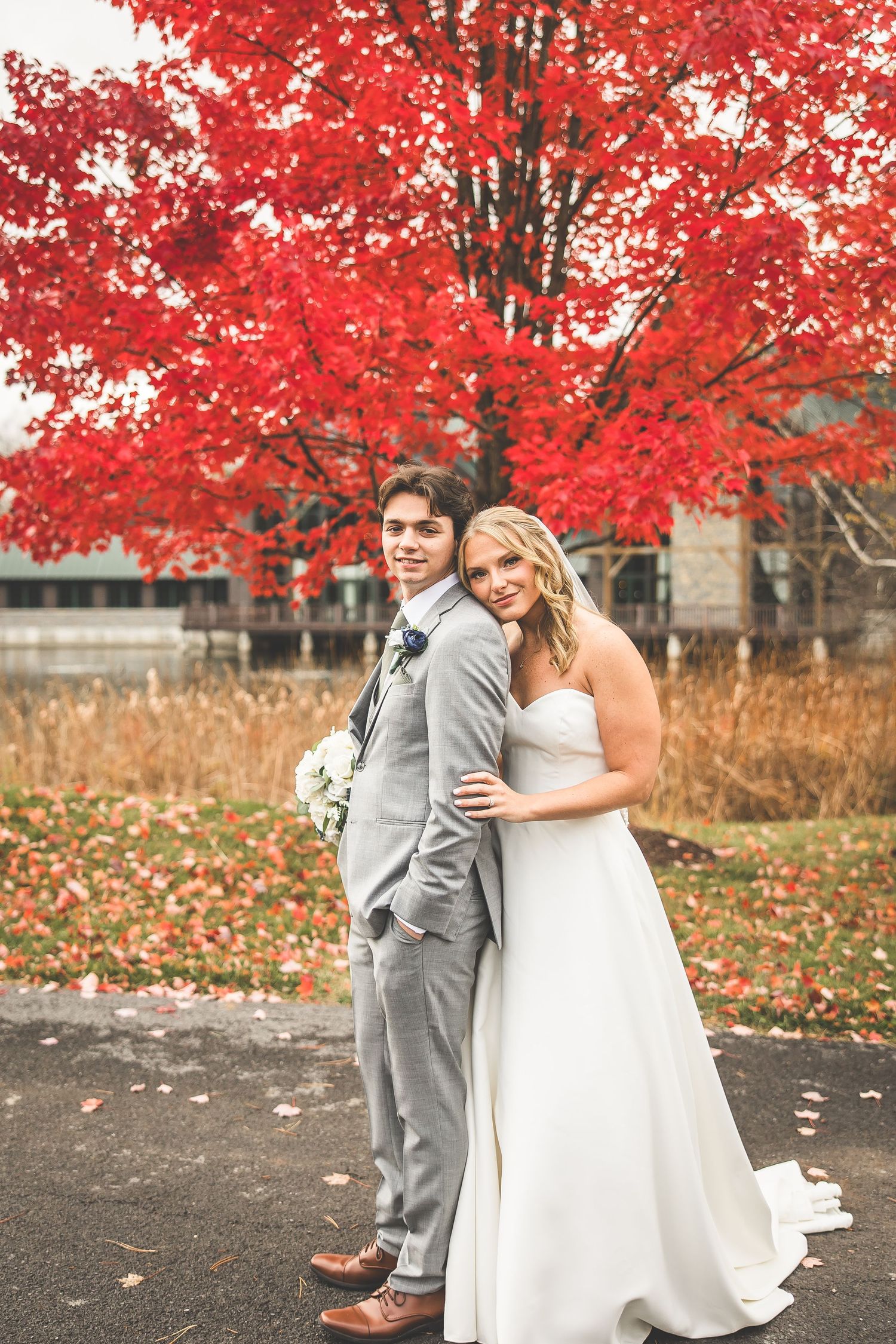 Newlyweds share intimate moments under bright red autumn foliage against a rustic backdrop.