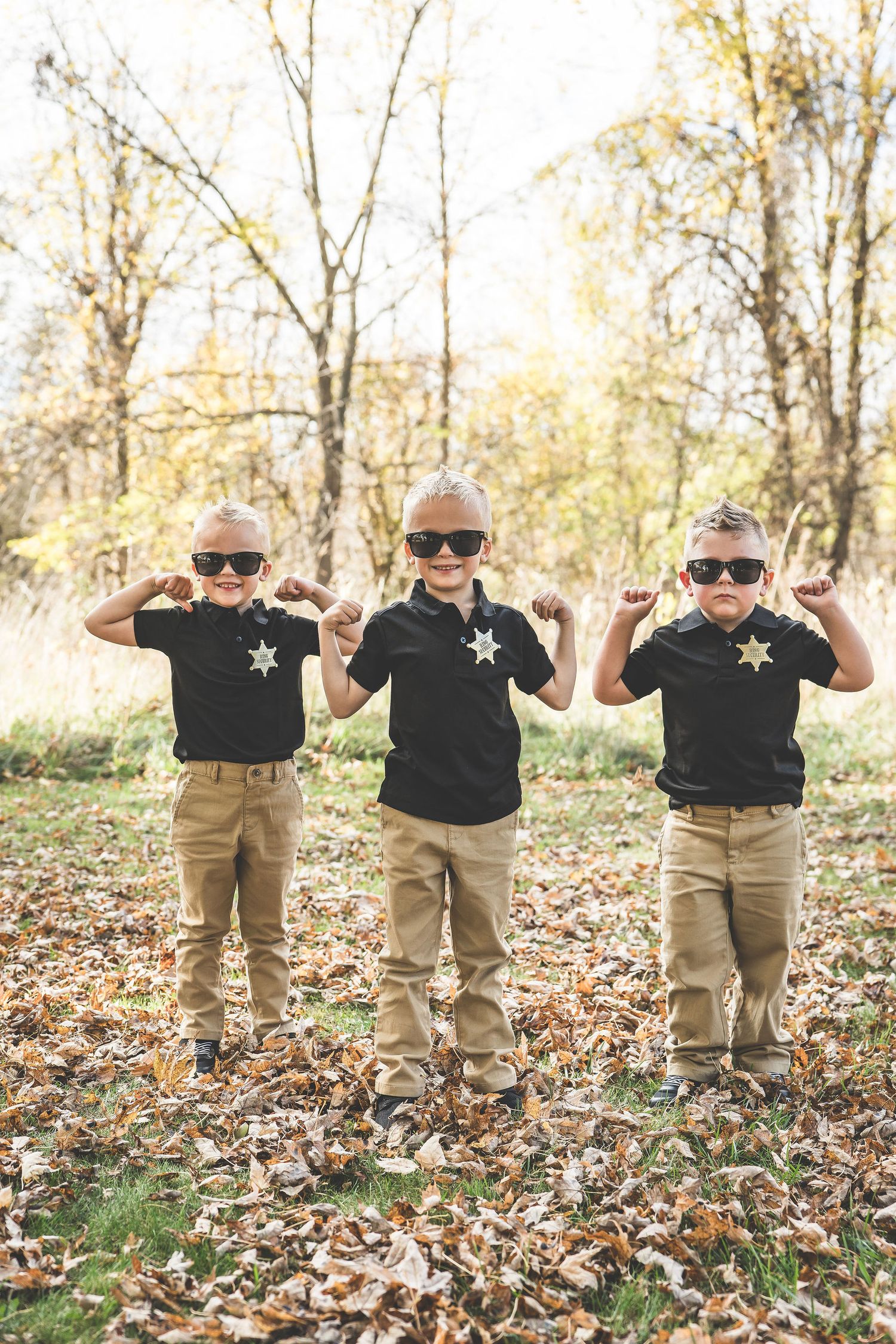 Three young boys in matching black polos and khakis strike poses while wearing sunglasses outdoors.