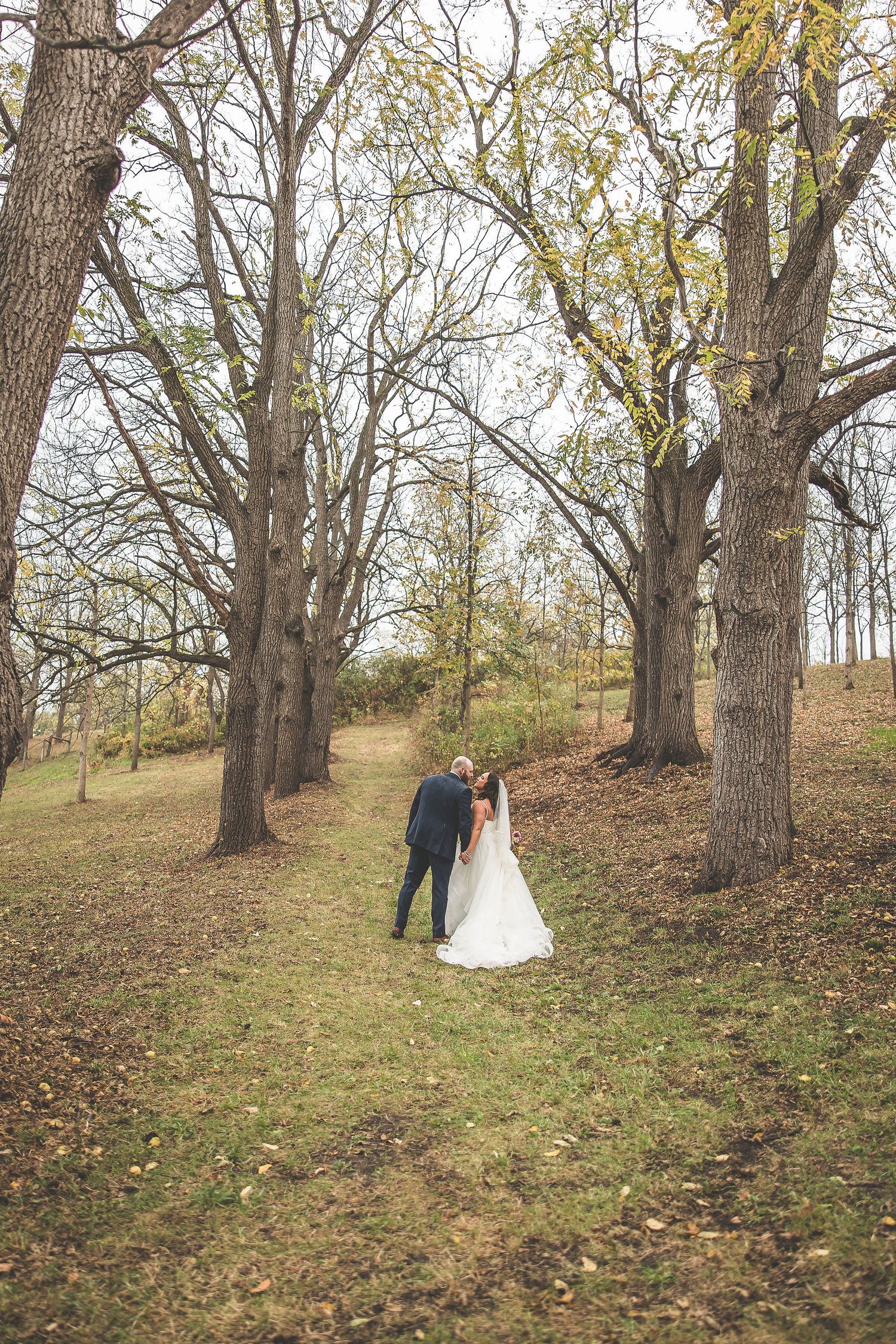 Wedding couple poses for romantic photos on a hillside surrounded by autumn trees.