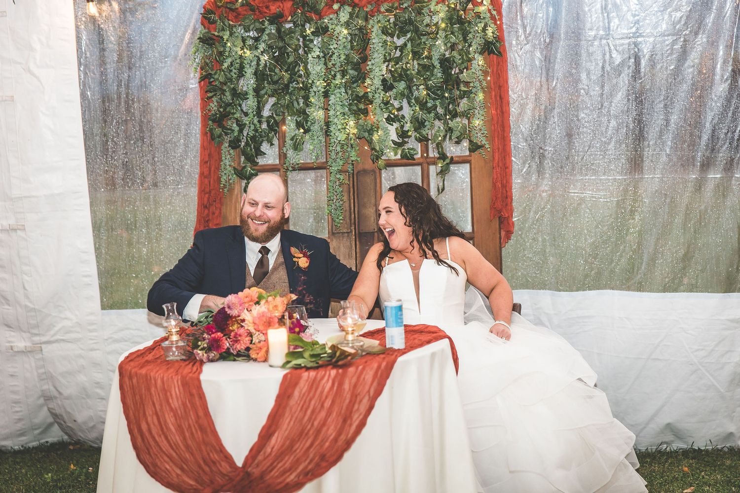 Sweetheart table setup with burgundy draping and greenery arch for wedding reception.