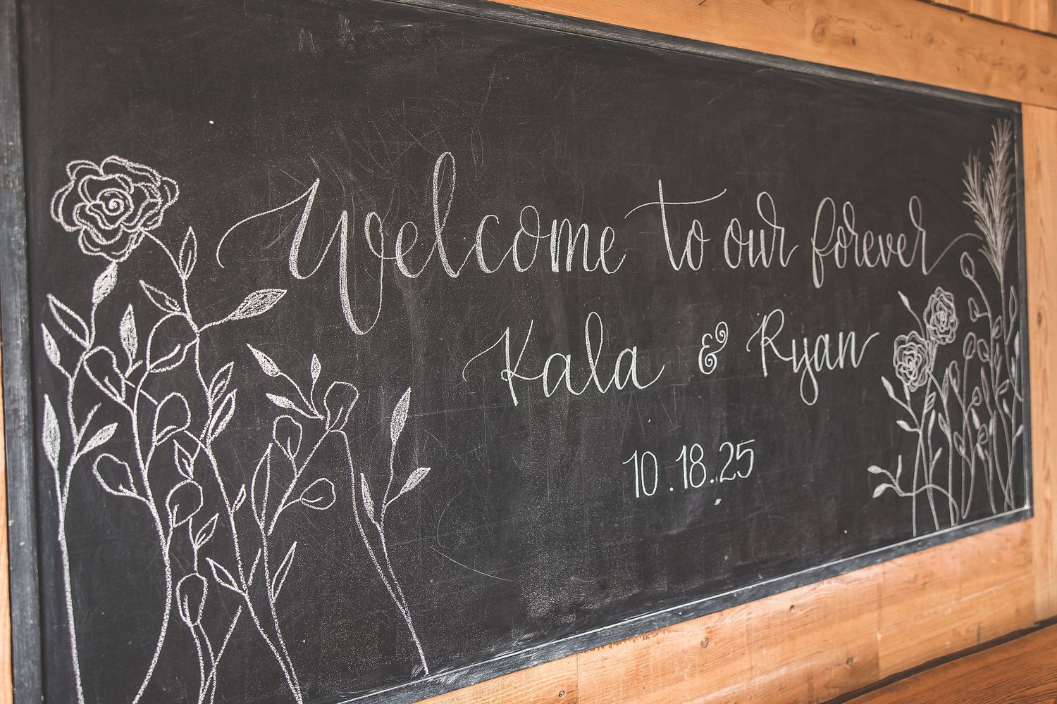 Long chalkboard with decorative wedding welcome message and artistic designs.