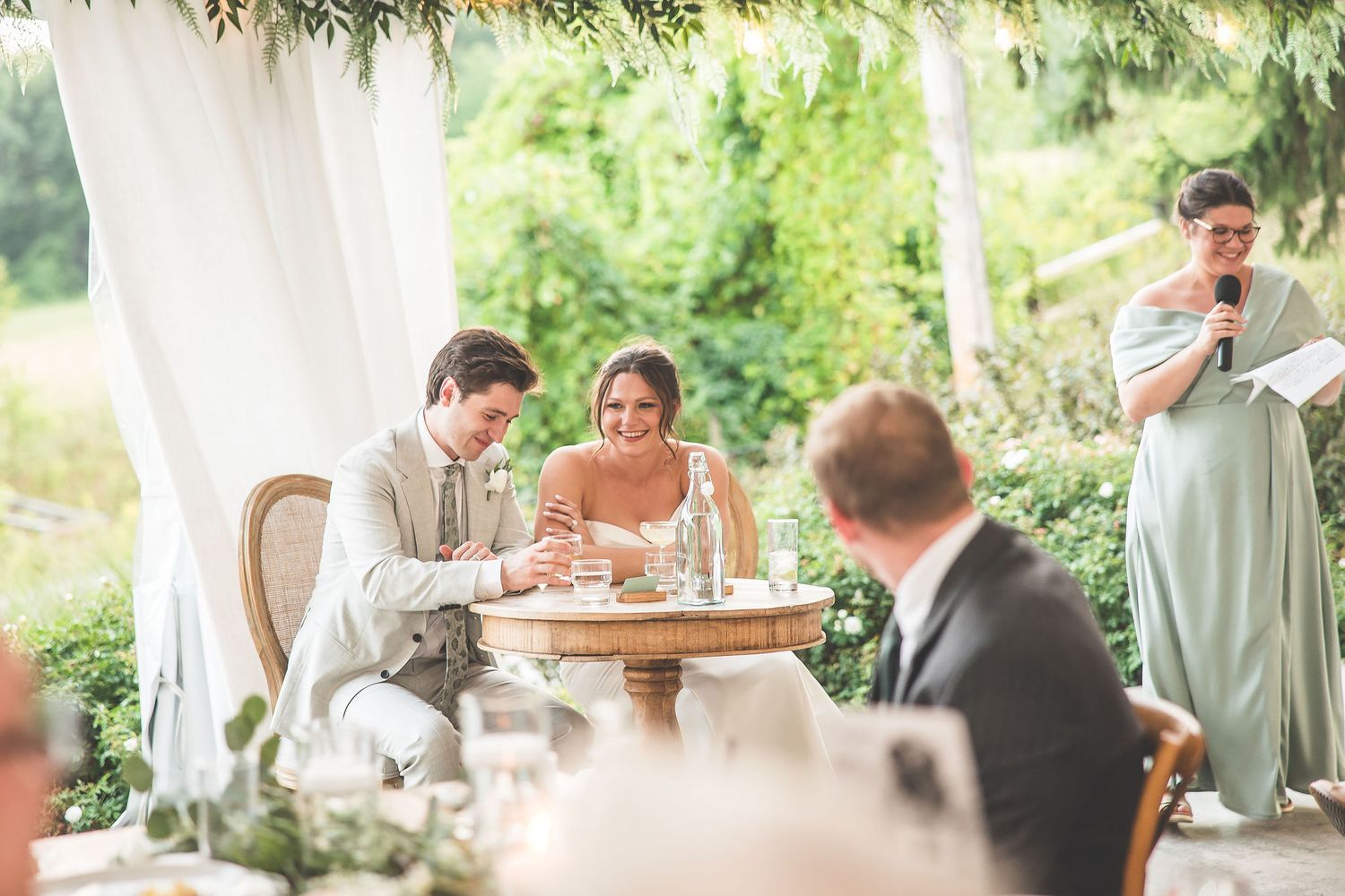 Wedding reception scene with speeches being given under an elegant white tent.