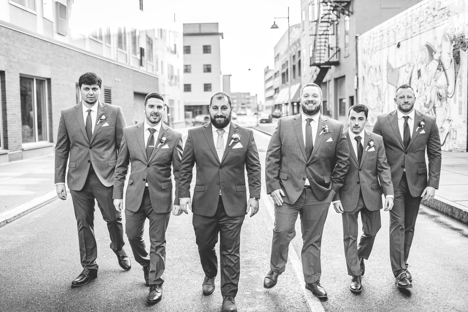 Wedding party groomsmen walking together down urban alley.