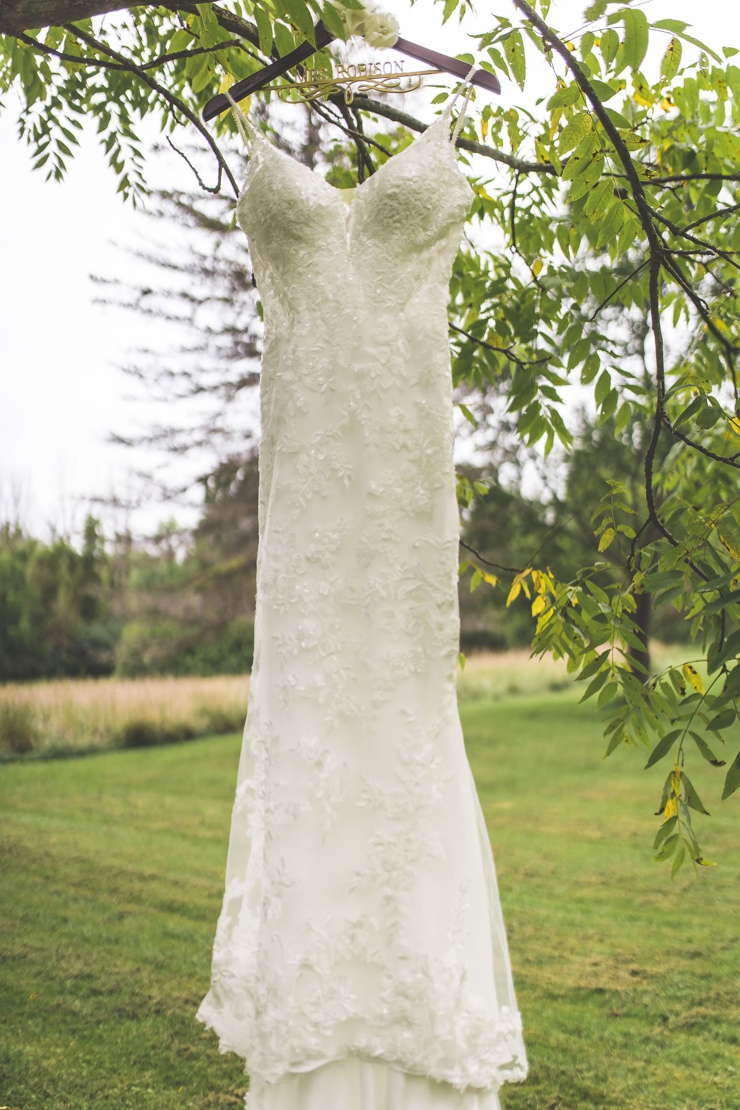 White lace wedding dress hanging from tree branches in a garden setting.