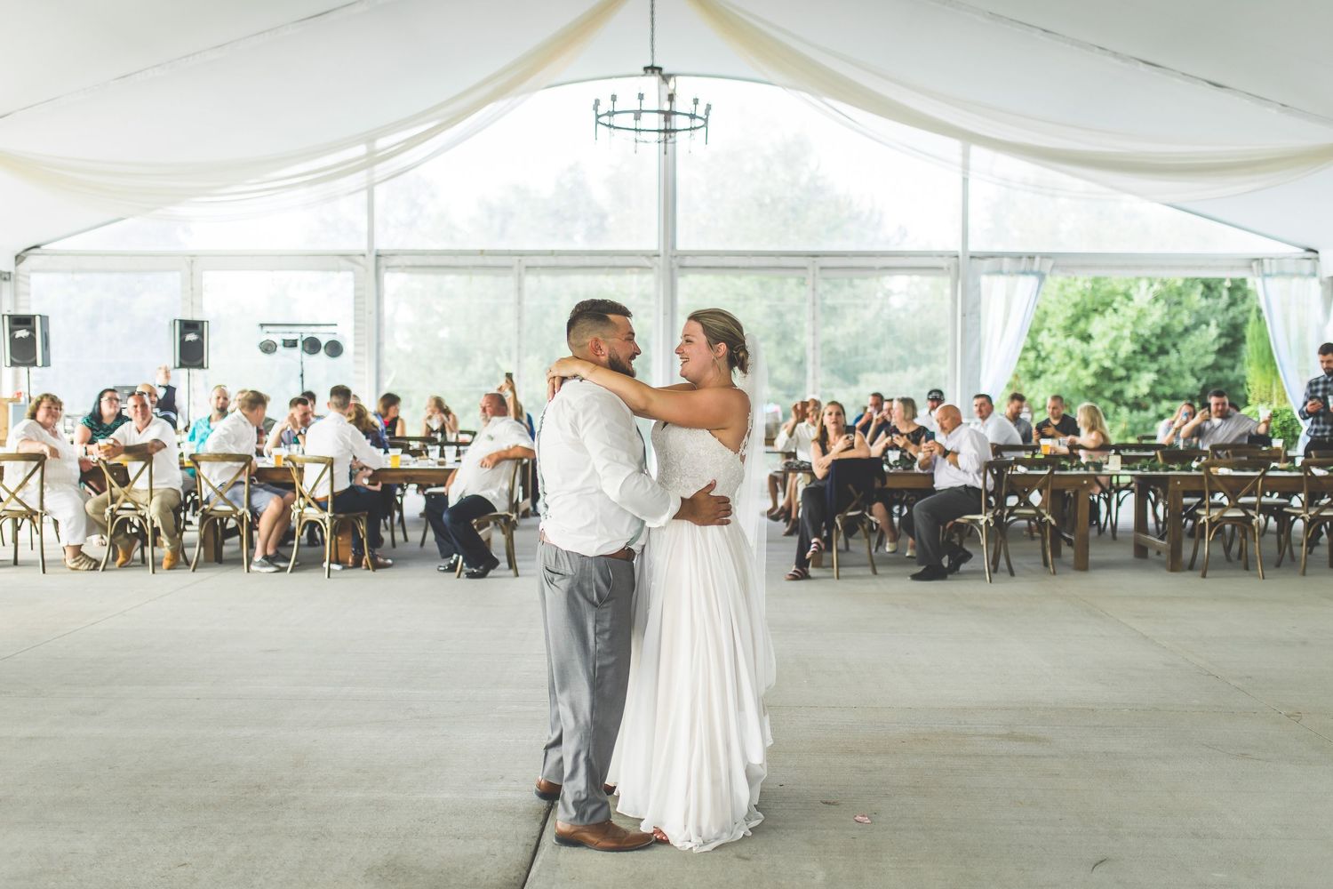 Wide angle view of a tented wedding reception with guests seated at wooden tables.