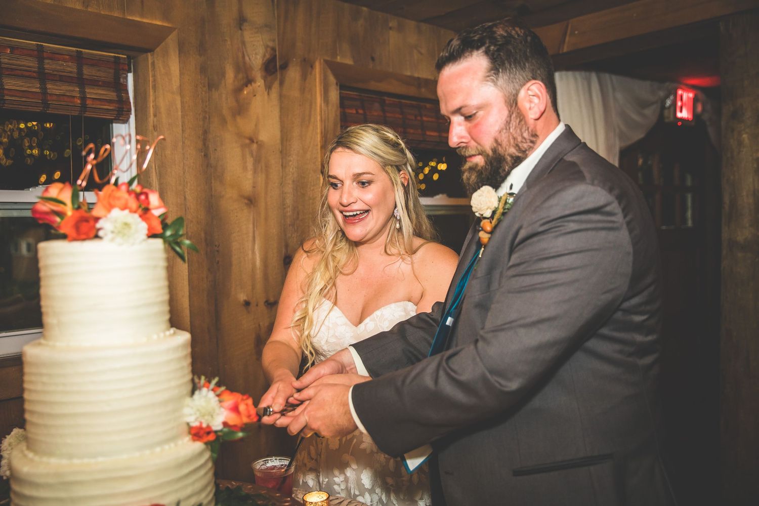 Newlyweds cut their elegant white tiered wedding cake in a rustic barn setting.