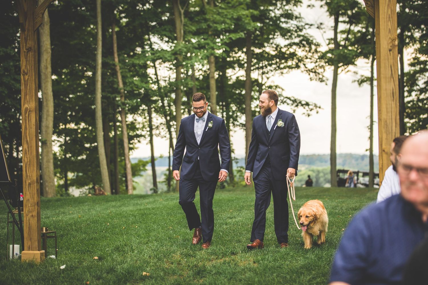 Wedding party members gathered outdoors between wooden posts.