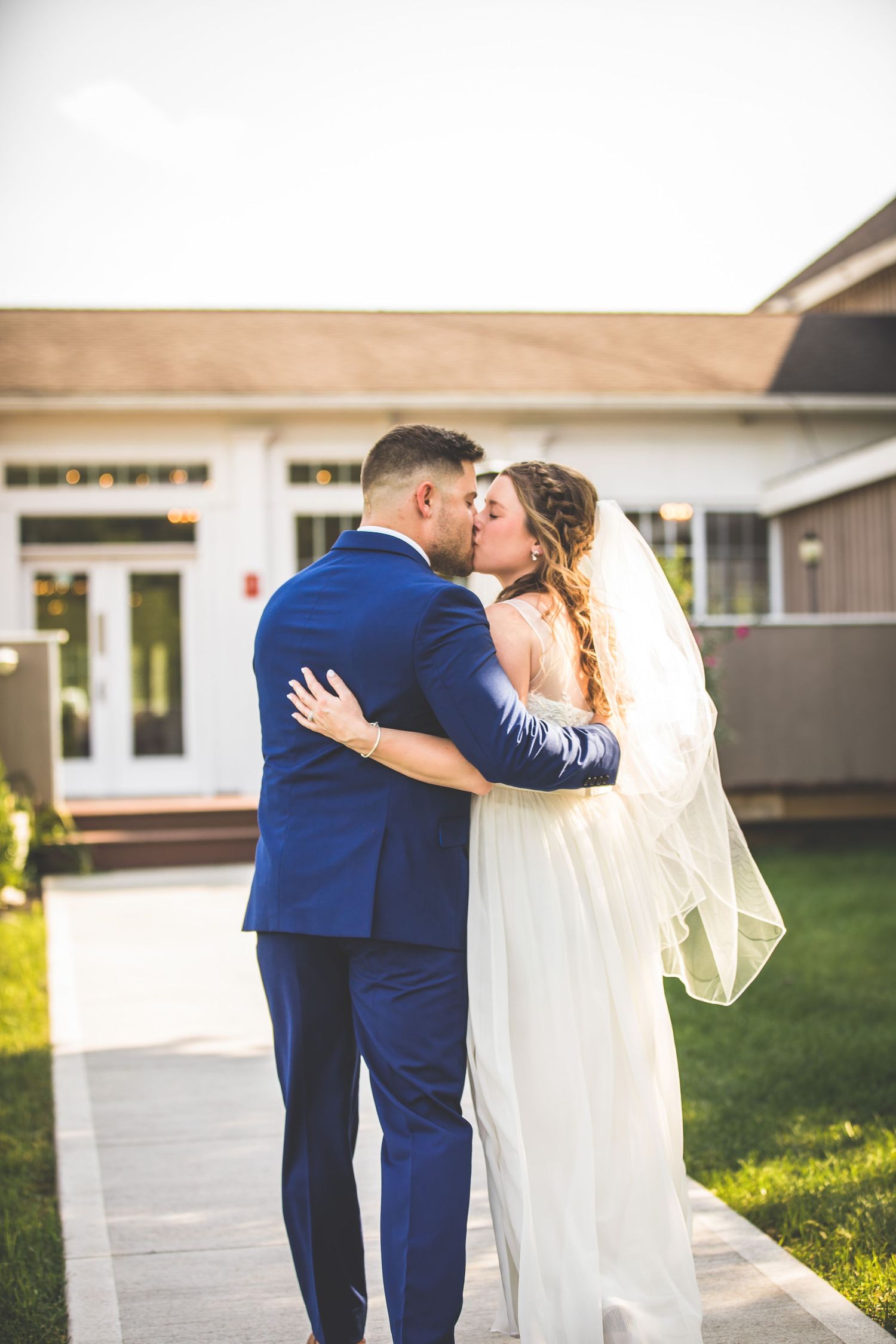 Newlyweds share an intimate moment outside a white building in classic wedding attire.