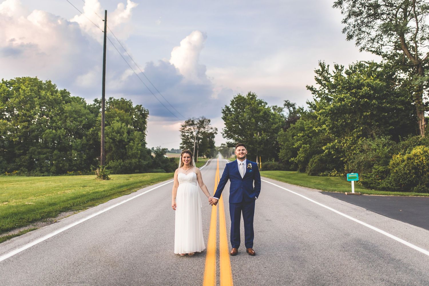 Wedding couple walking along rural road with dramatic clouds overhead.