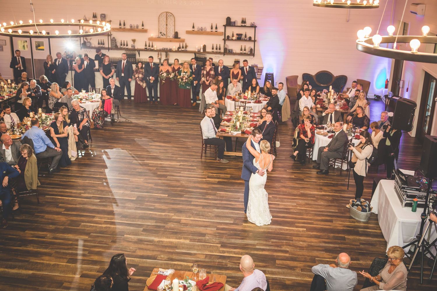 Large wedding reception venue filled with guests at round tables during evening celebration.