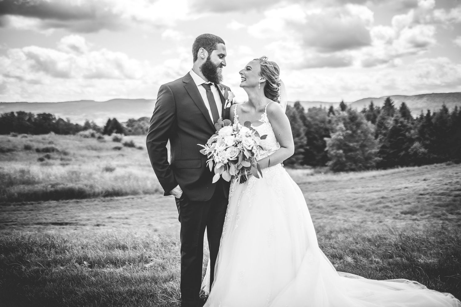 Black and white wedding photo of a couple sharing an intimate moment on a hilltop.