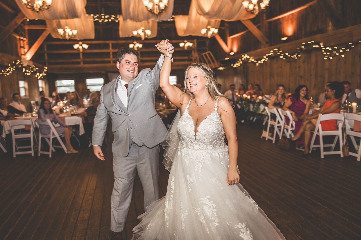 Couple shares intimate dance moment in barn venue decorated with twinkling lights and white fabric.