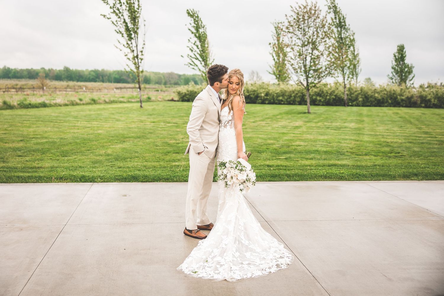 Wedding couple poses together on a concrete path surrounded by green landscape.