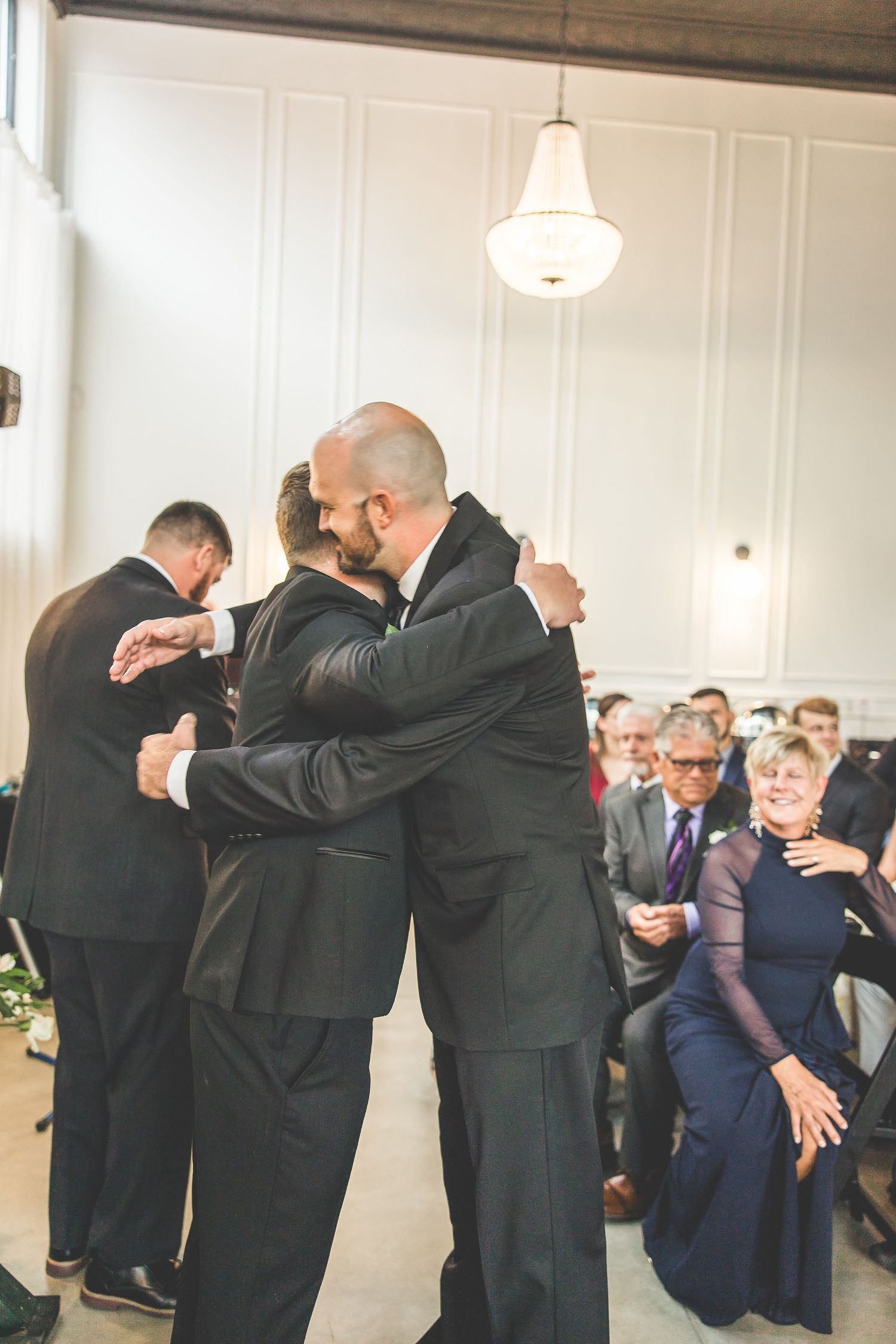 Groomsmen share emotional embraces in a touching group moment at the wedding.