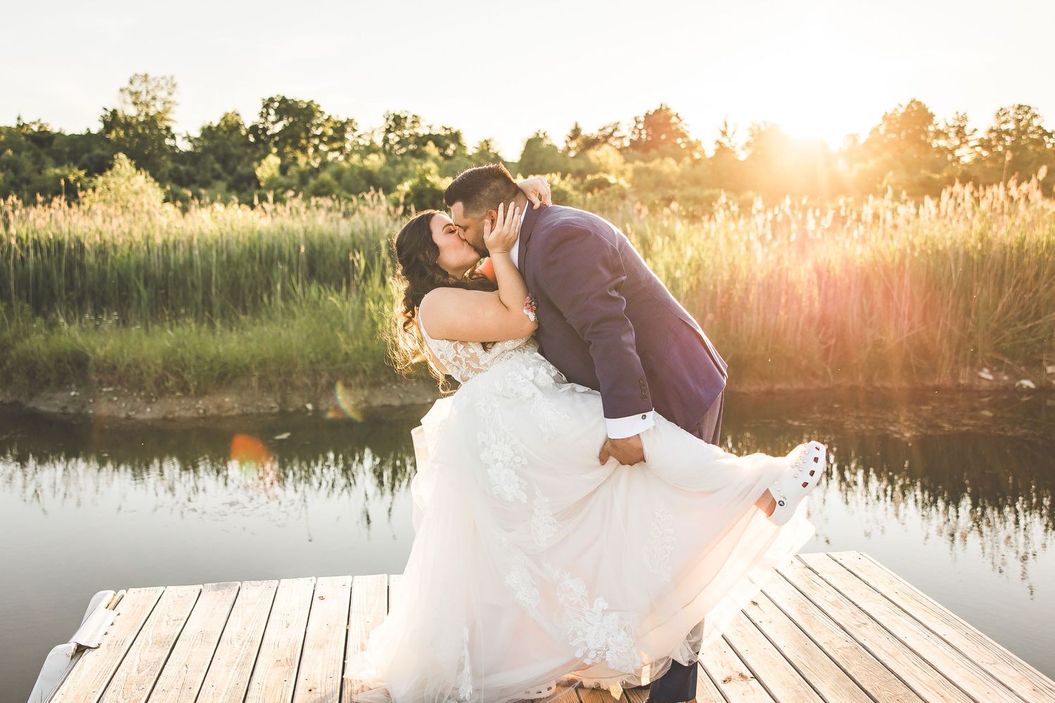 Sunset wedding photos on wooden dock by tranquil lake.