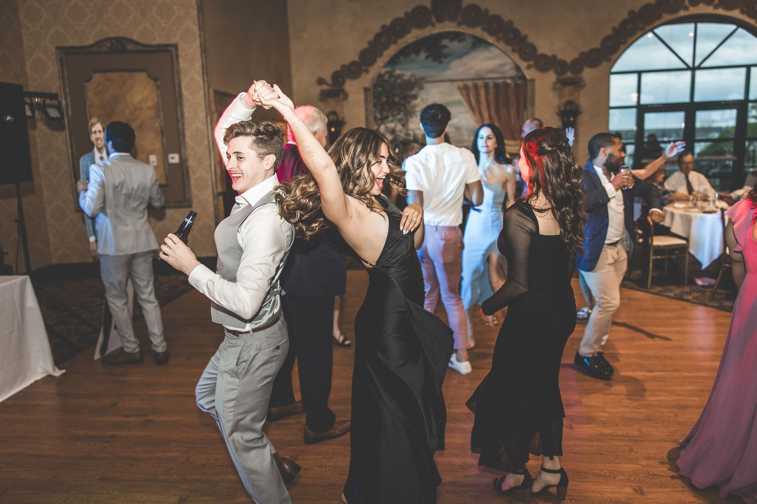 Wedding reception dance floor filled with guests celebrating under arched windows.