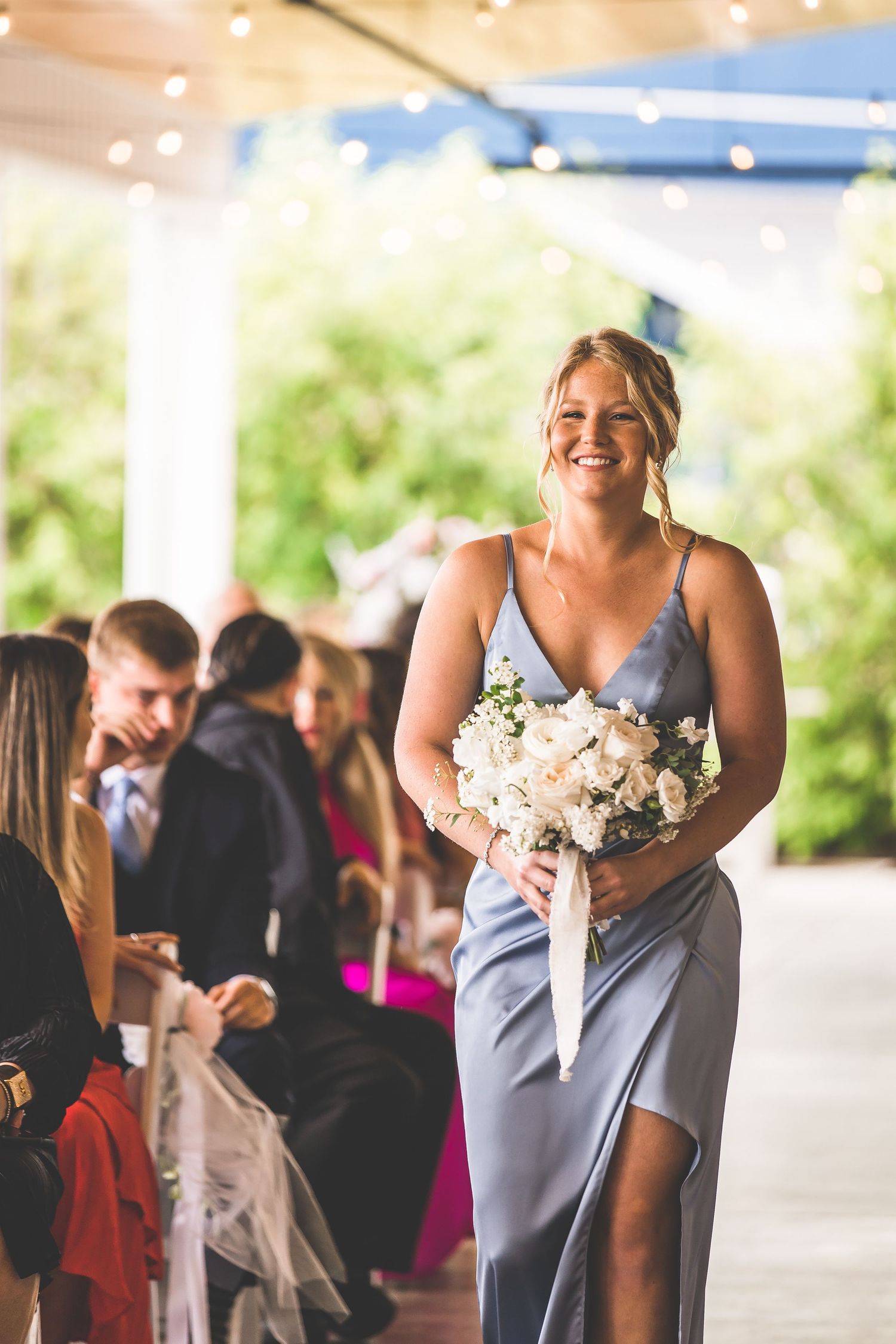 Bridesmaids in light blue dresses walk down the aisle carrying white floral bouquets.