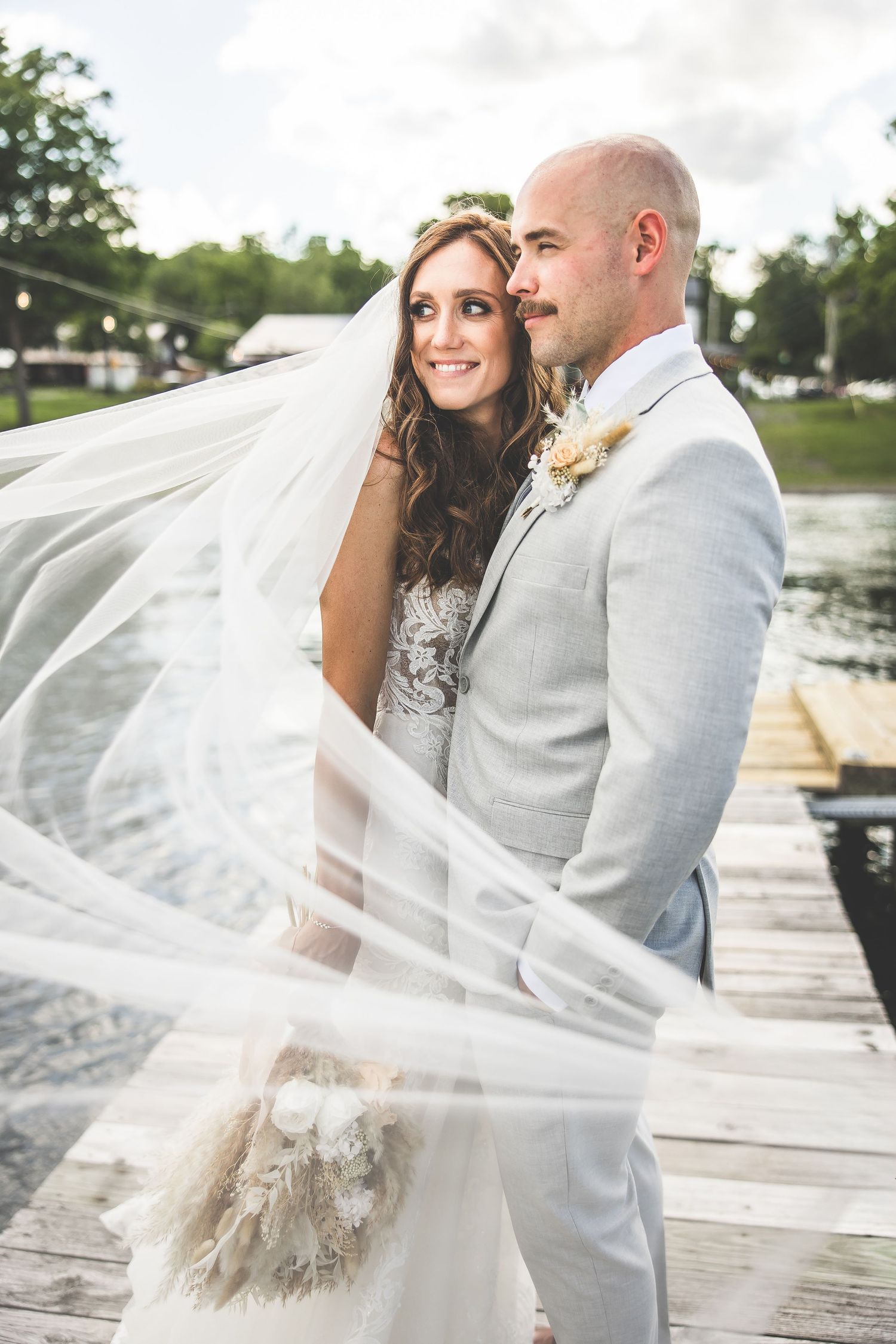 Couple shares intimate moments on a dock with bride's veil flowing in the breeze.