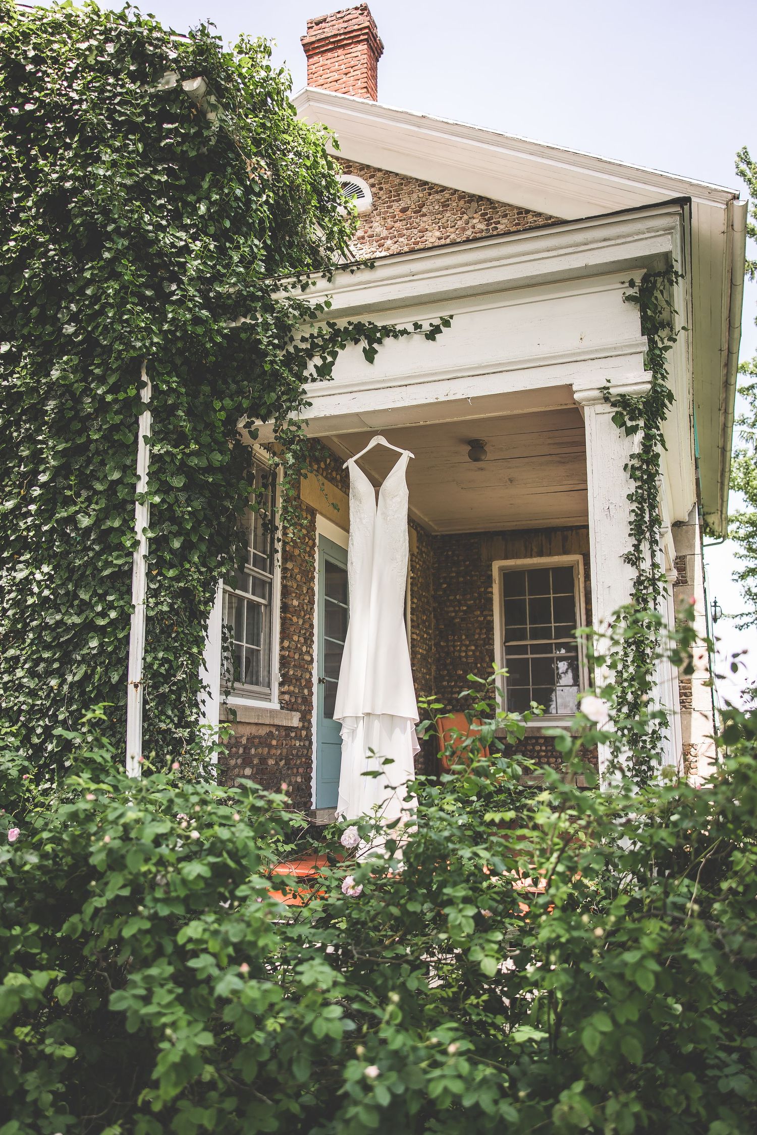 White porch of a stone house with climbing ivy and elegant columns.