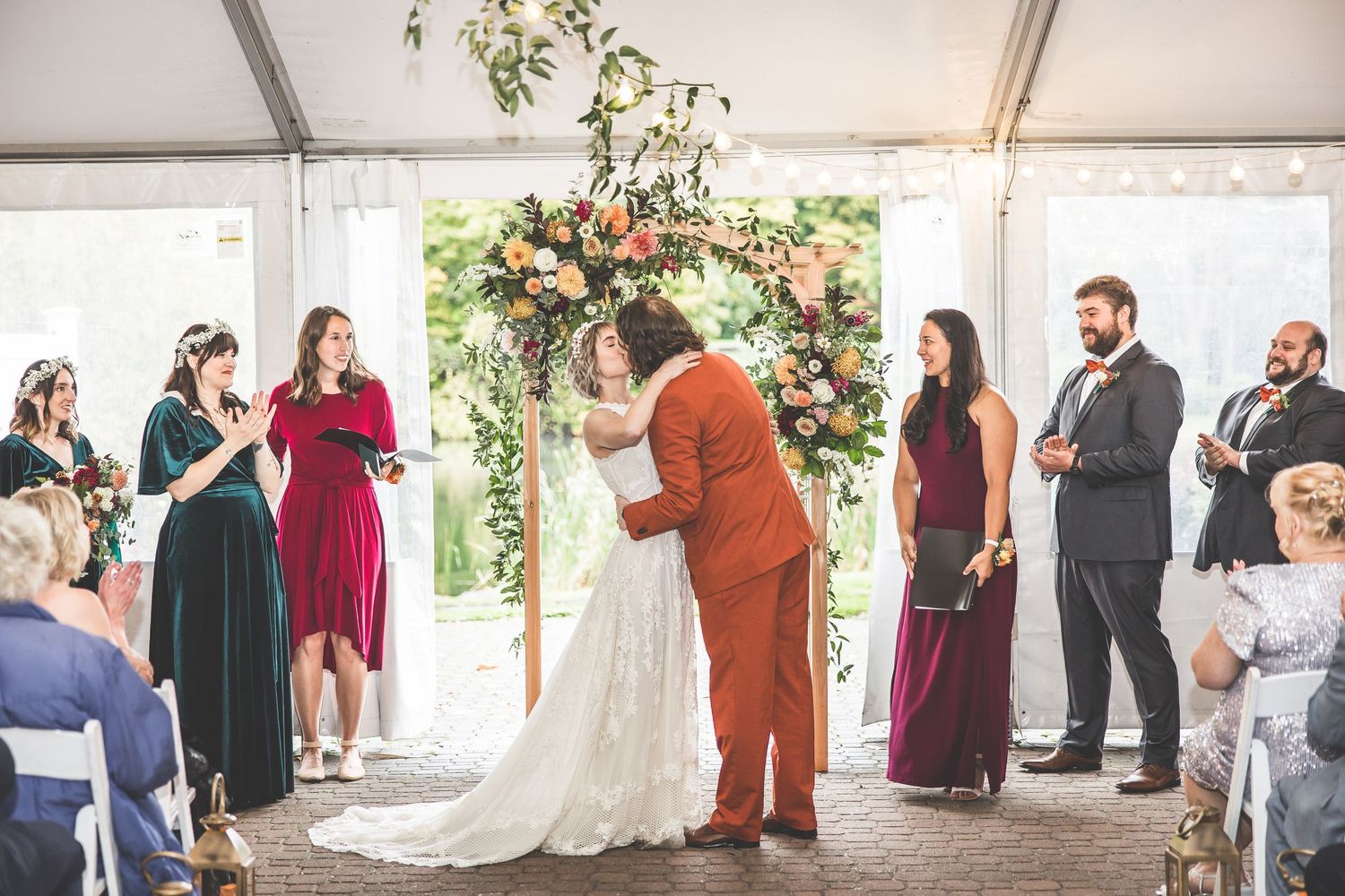 Wedding celebration in white tent venue with floral decorations and gathered guests.