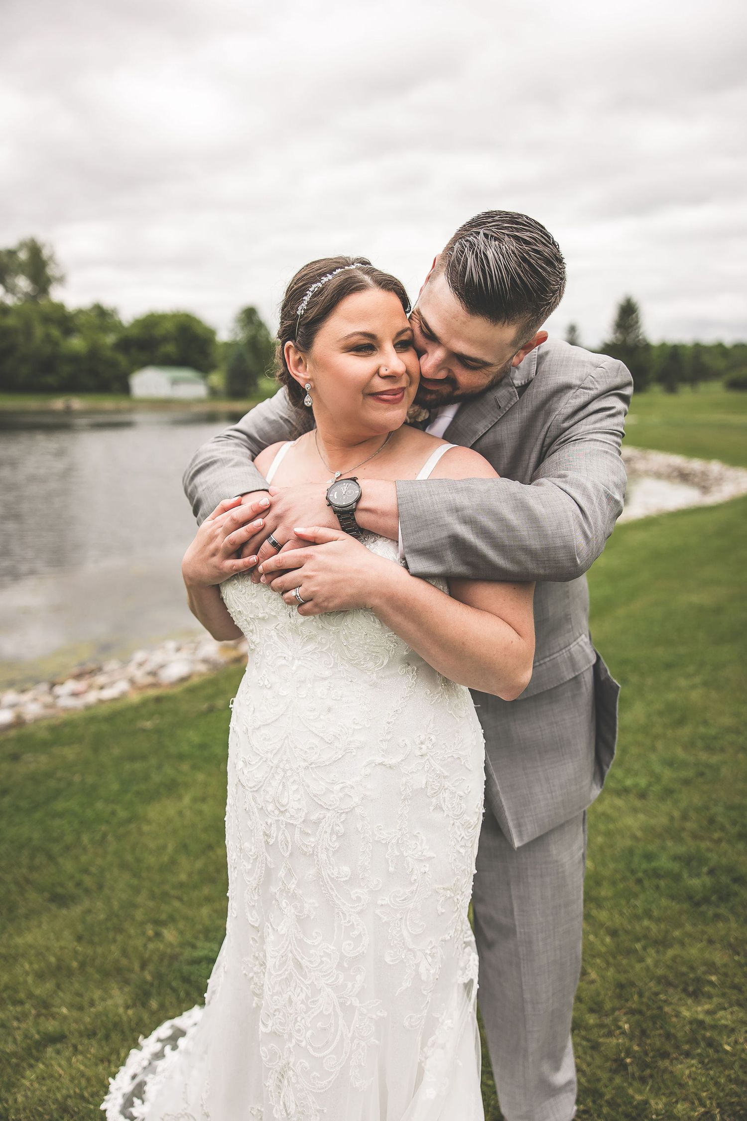 A tender embrace between newlyweds on a scenic golf course with a pond in the background.